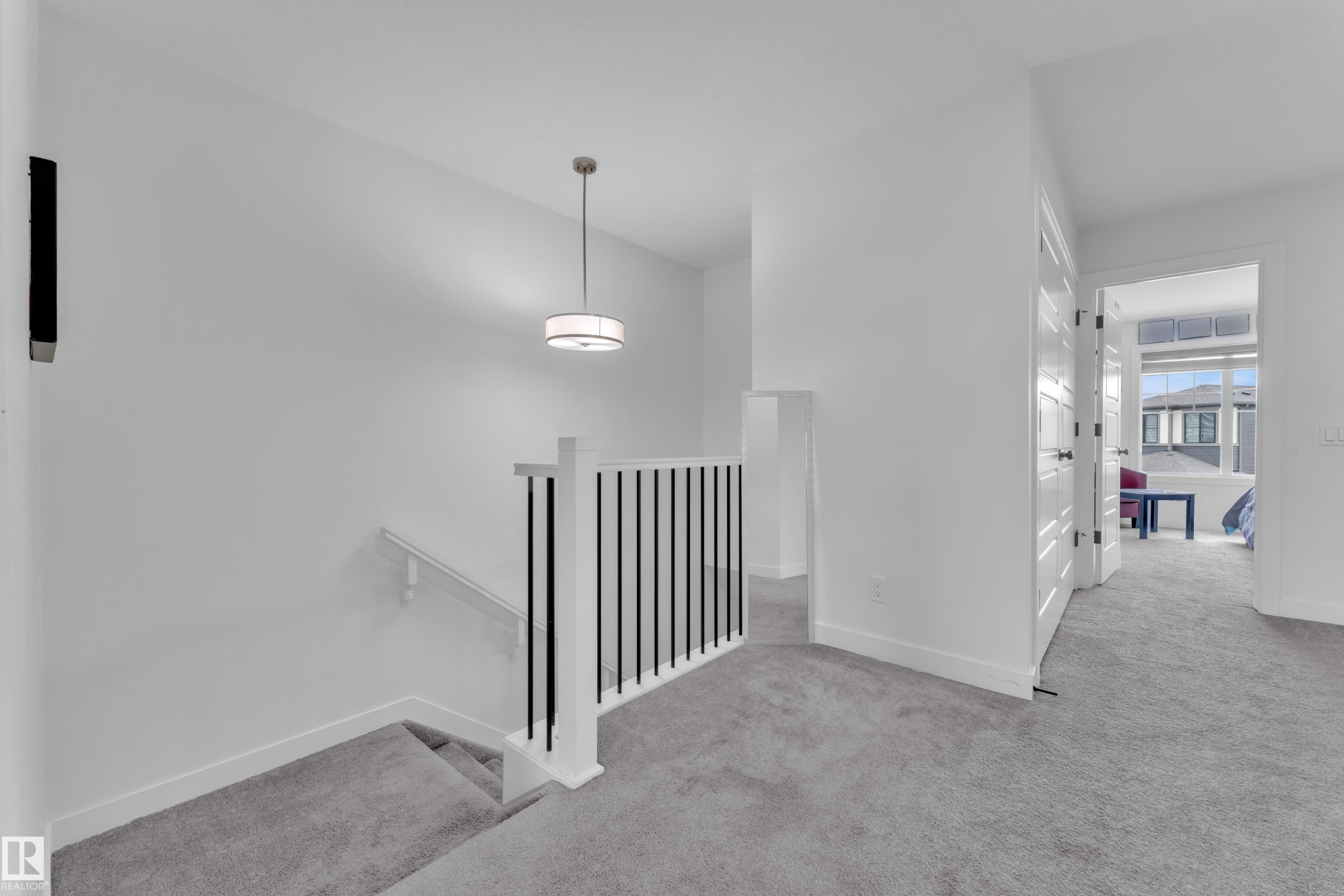 Upper-level landing featuring light gray carpeting, white walls, a contemporary drum pendant light, and a staircase with white newel posts and black balusters - 1645 Plum Circle Circle Sw, Edmonton, AB - Indoor Photo Showing Other Room