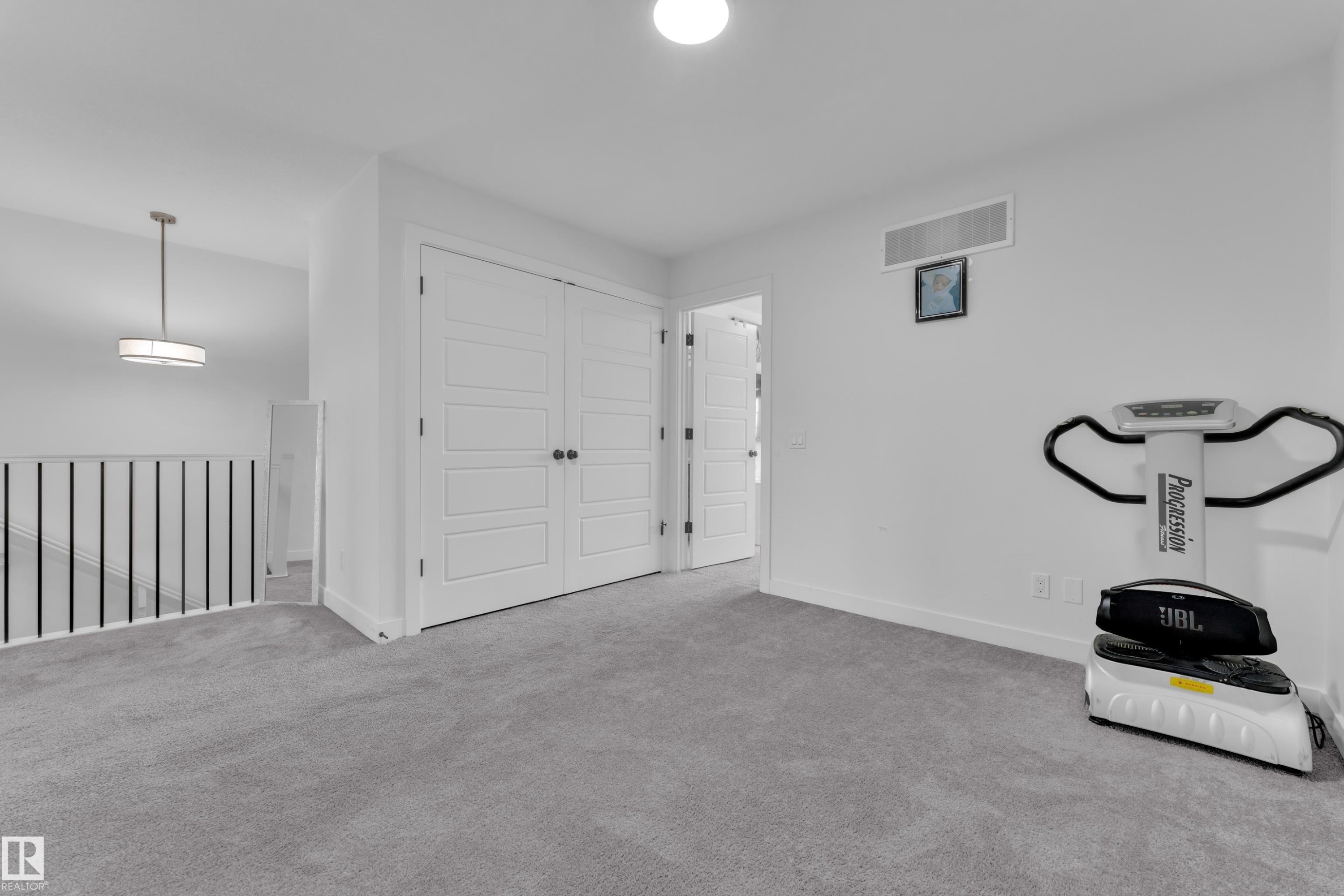 Carpeted loft space featuring white paneled double doors, a contemporary drum pendant light fixture, and a white baluster railing - 1645 Plum Circle Circle Sw, Edmonton, AB - Indoor Photo Showing Other Room