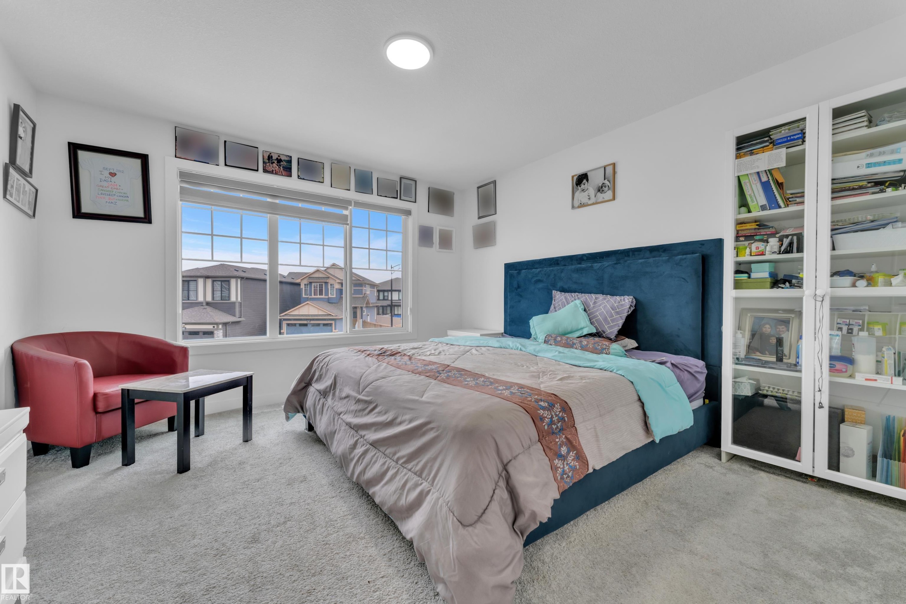 Bright bedroom featuring a large window with white grid panes, light-colored carpeting, a built-in white bookshelf with glass doors, and recessed ceiling lighting - 1645 Plum Circle Circle Sw, Edmonton, AB - Indoor Photo Showing Bedroom