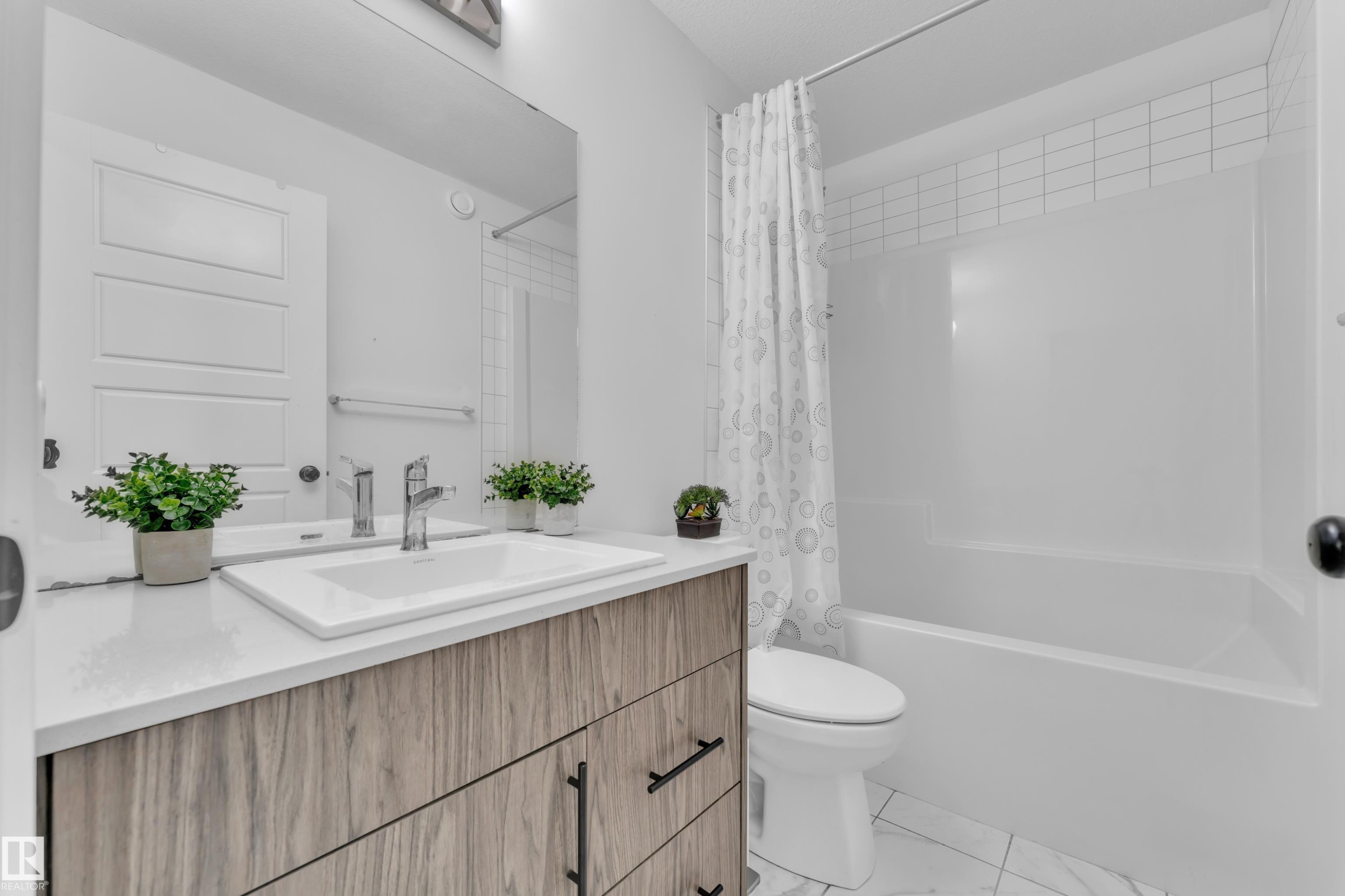 Bathroom featuring a wood-finish vanity with a white countertop and undermount sink, chrome faucet, and rectangular mirror - 1645 Plum Circle Circle Sw, Edmonton, AB - Indoor Photo Showing Bathroom