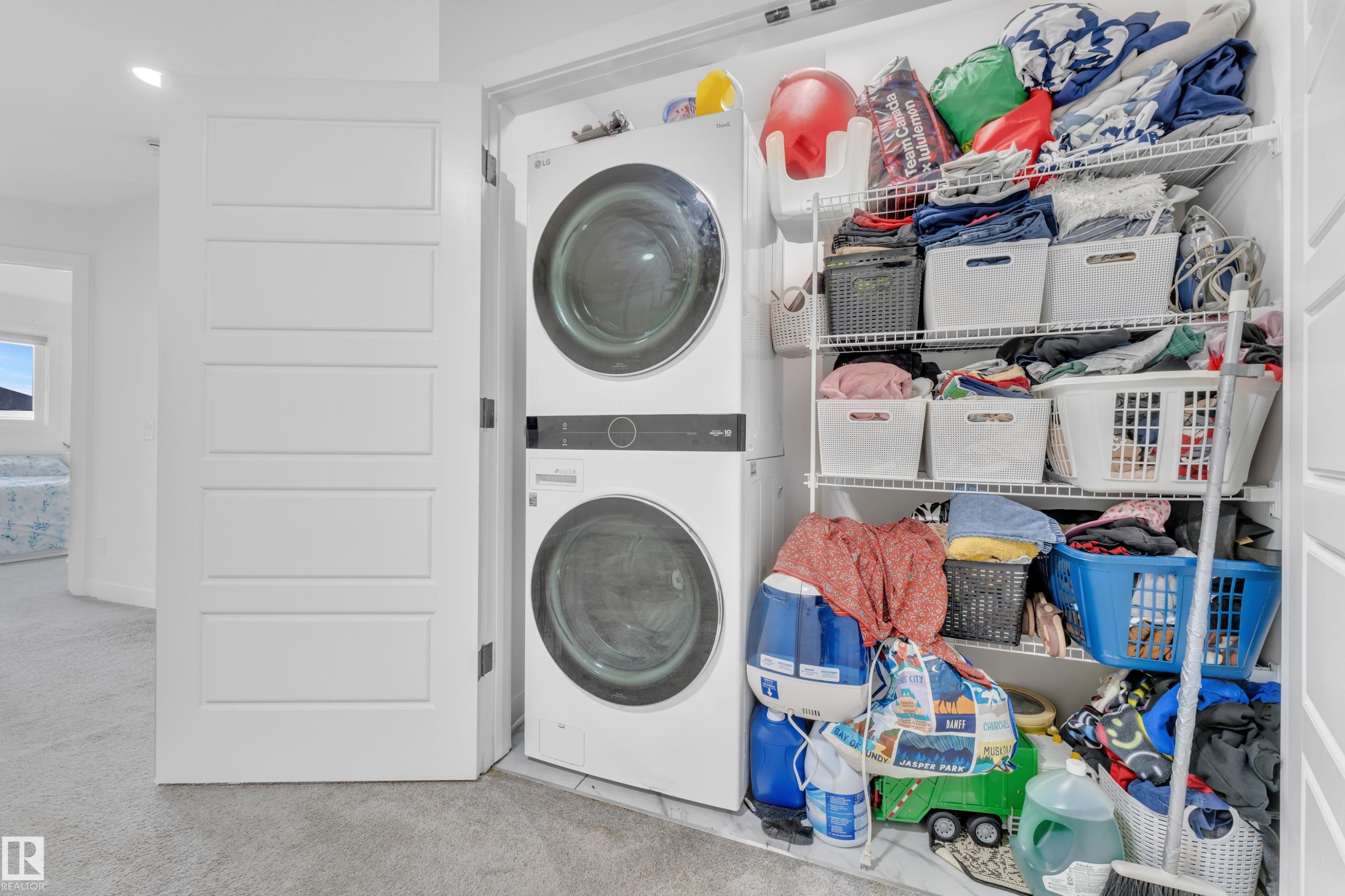 Dedicated laundry closet featuring a stacked washer and dryer unit, multiple wire shelving units, and a modern five-panel interior door - 1645 Plum Circle Circle Sw, Edmonton, AB - Indoor Photo Showing Laundry Room