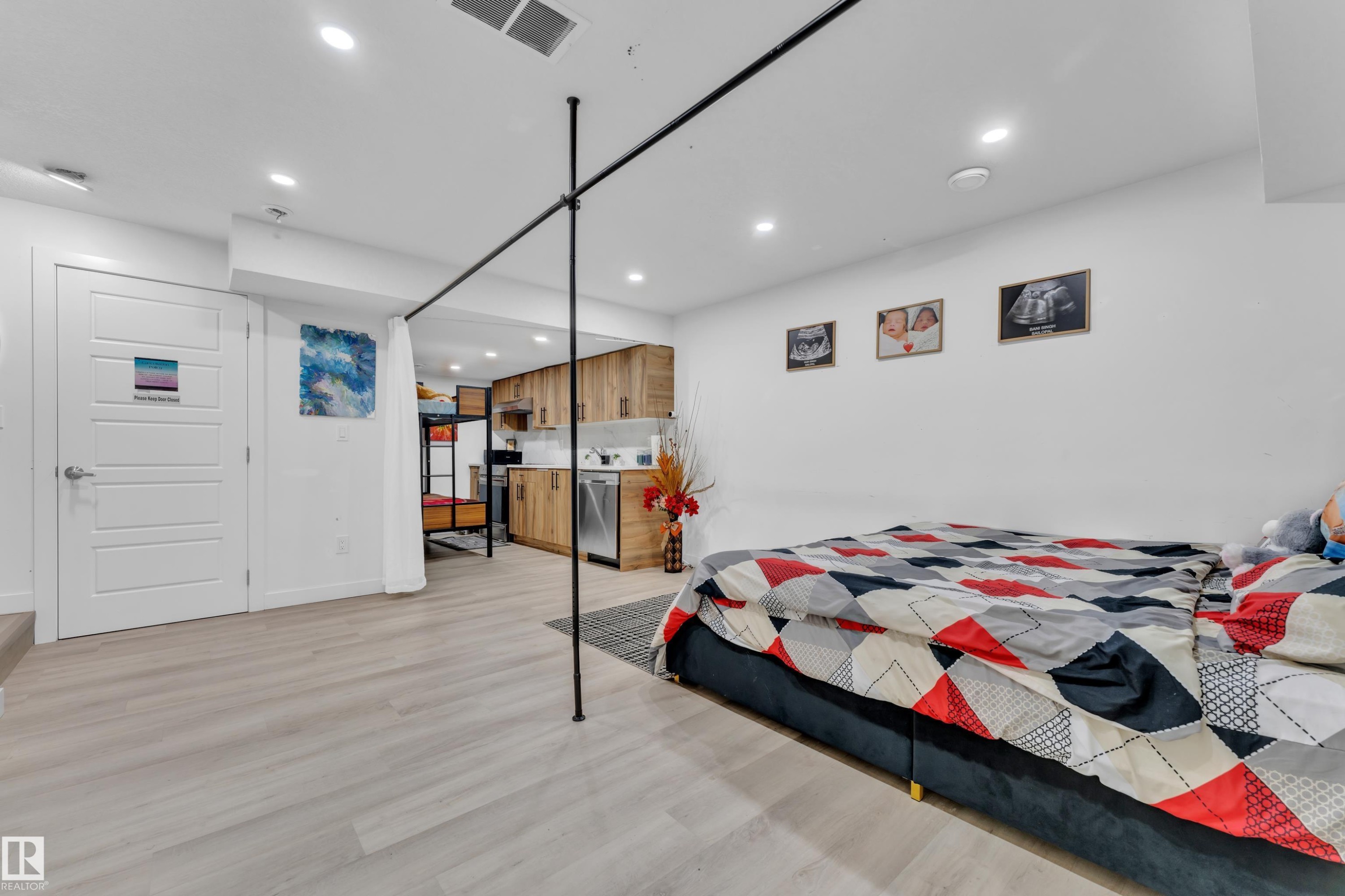 Open-concept living area with light wood-finish flooring, recessed lighting, white walls, and a visible kitchen featuring wood cabinetry and stainless steel appliances - 1645 Plum Circle Circle Sw, Edmonton, AB - Indoor Photo Showing Bedroom