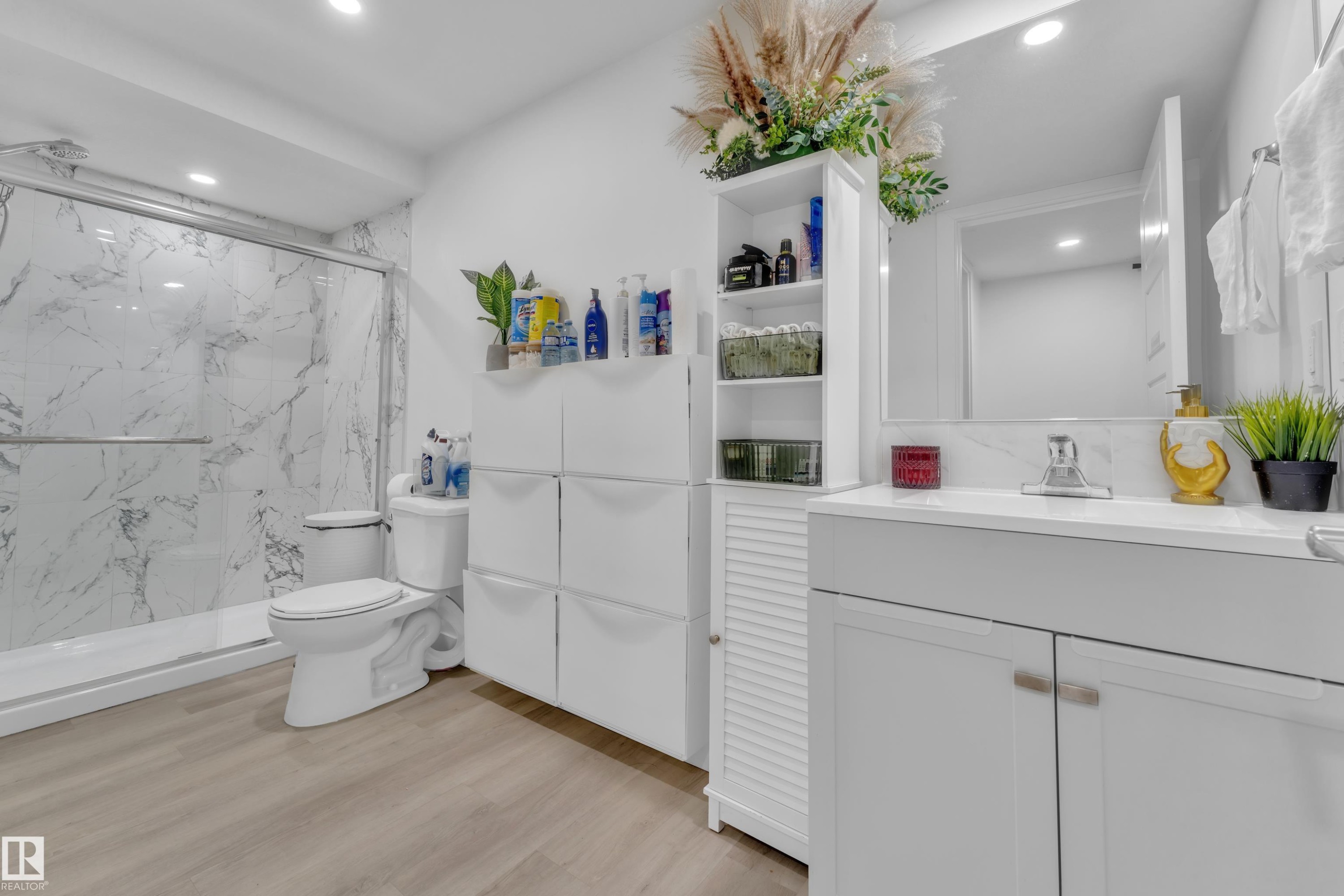 Bathroom featuring a white vanity with an undermount sink, a mirrored medicine cabinet, a walk-in shower with a glass enclosure and marble-patterned wall tiles, and wood-finish flooring - 1645 Plum Circle Circle Sw, Edmonton, AB - Indoor Photo Showing Bathroom