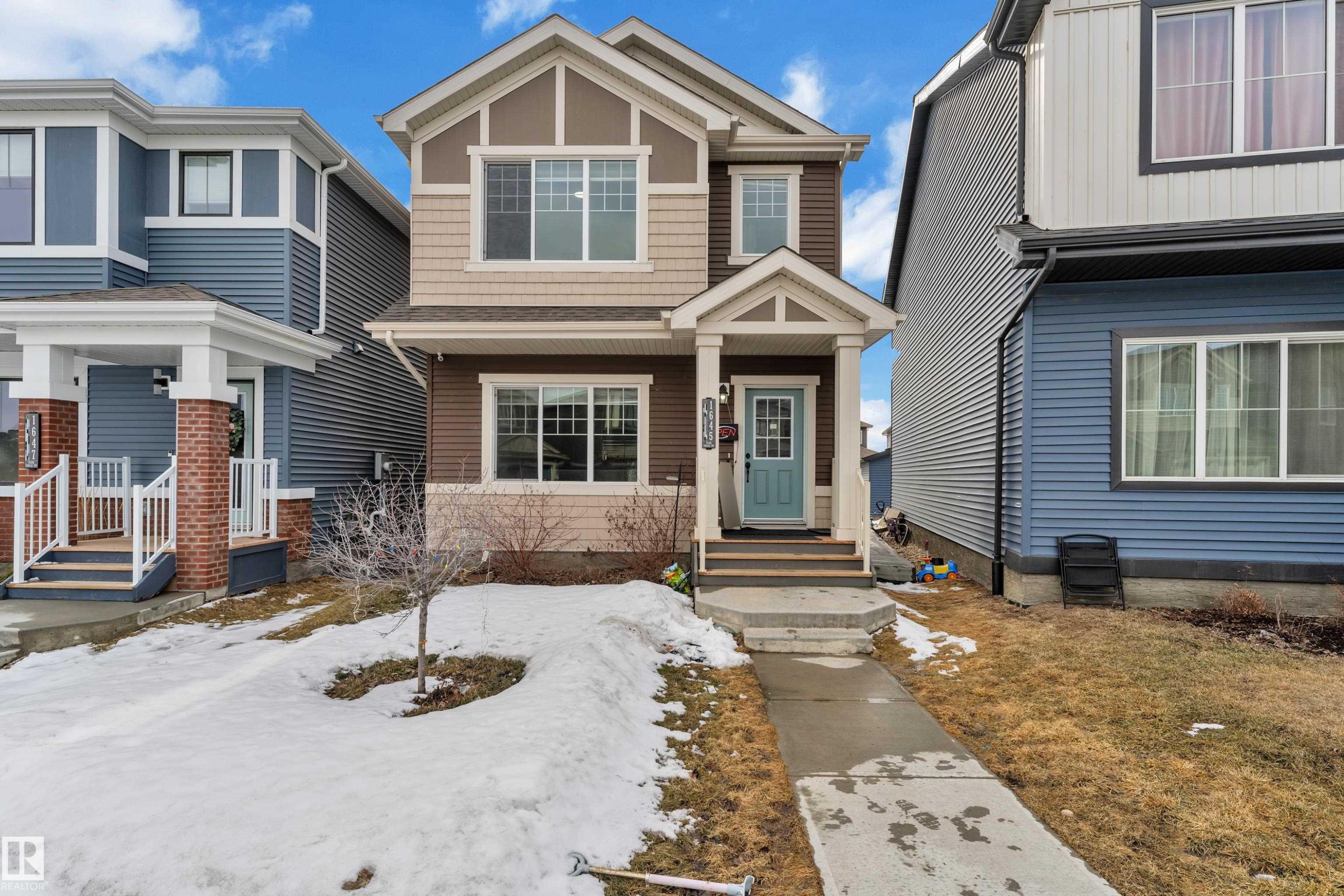 Two-story residence featuring a covered front entry, light blue paneled front door, and a multi-tone exterior with brown siding, beige shingles, and white trim - 1645 Plum Circle Circle Sw, Edmonton, AB - Outdoor With Facade