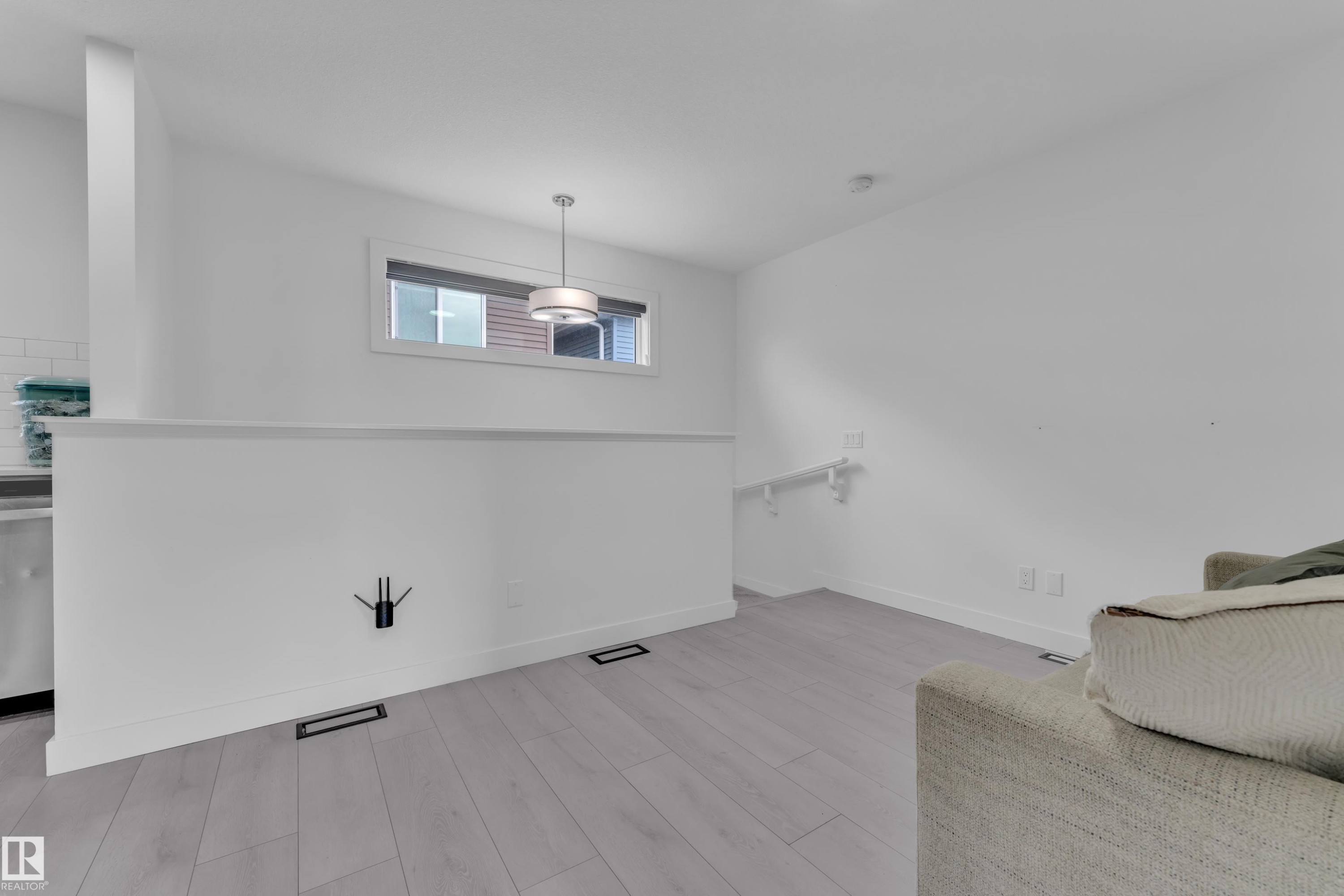 Open concept living area featuring light wood-finish flooring, a contemporary pendant light fixture, and a partial wall separating spaces - 1645 Plum Circle Circle Sw, Edmonton, AB - Indoor Photo Showing Other Room