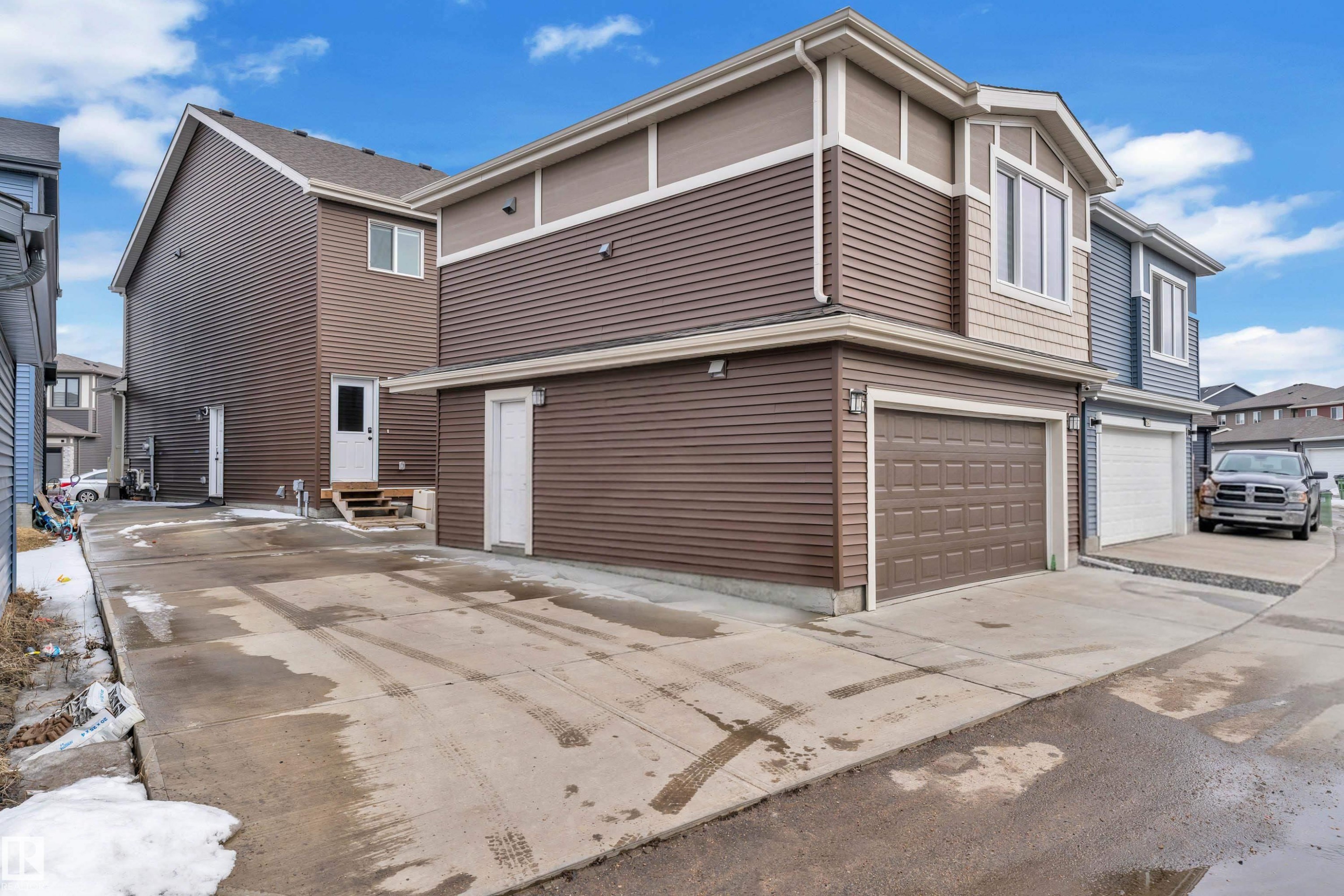 Two-story residence featuring brown and beige siding, an attached garage with a brown panel door, and a concrete driveway - 1645 Plum Circle Circle Sw, Edmonton, AB - Outdoor