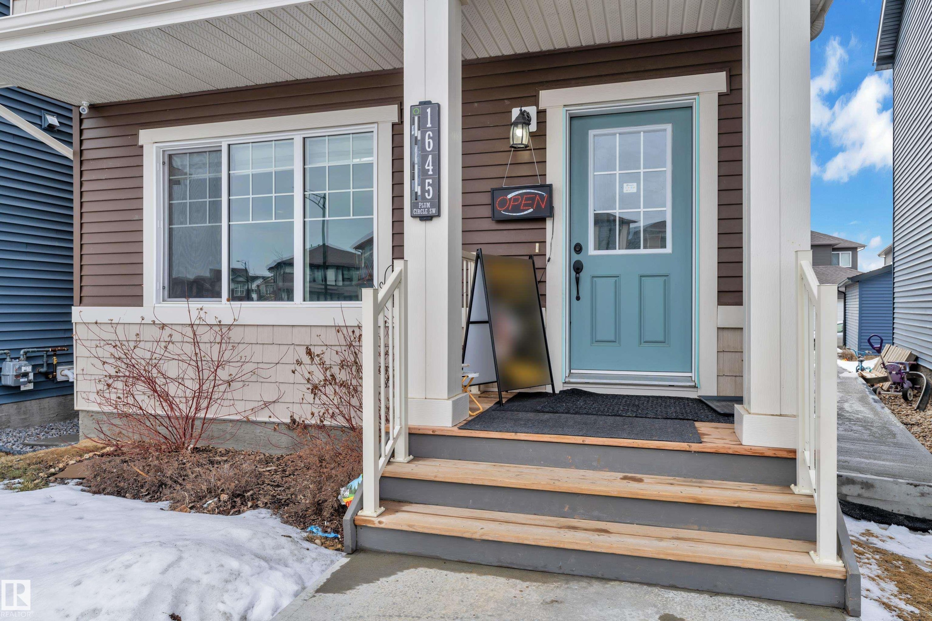 Inviting front entrance featuring a light blue door with gridded glass, wood-finish steps, and a white railing - 1645 Plum Circle Circle Sw, Edmonton, AB - Outdoor With Exterior