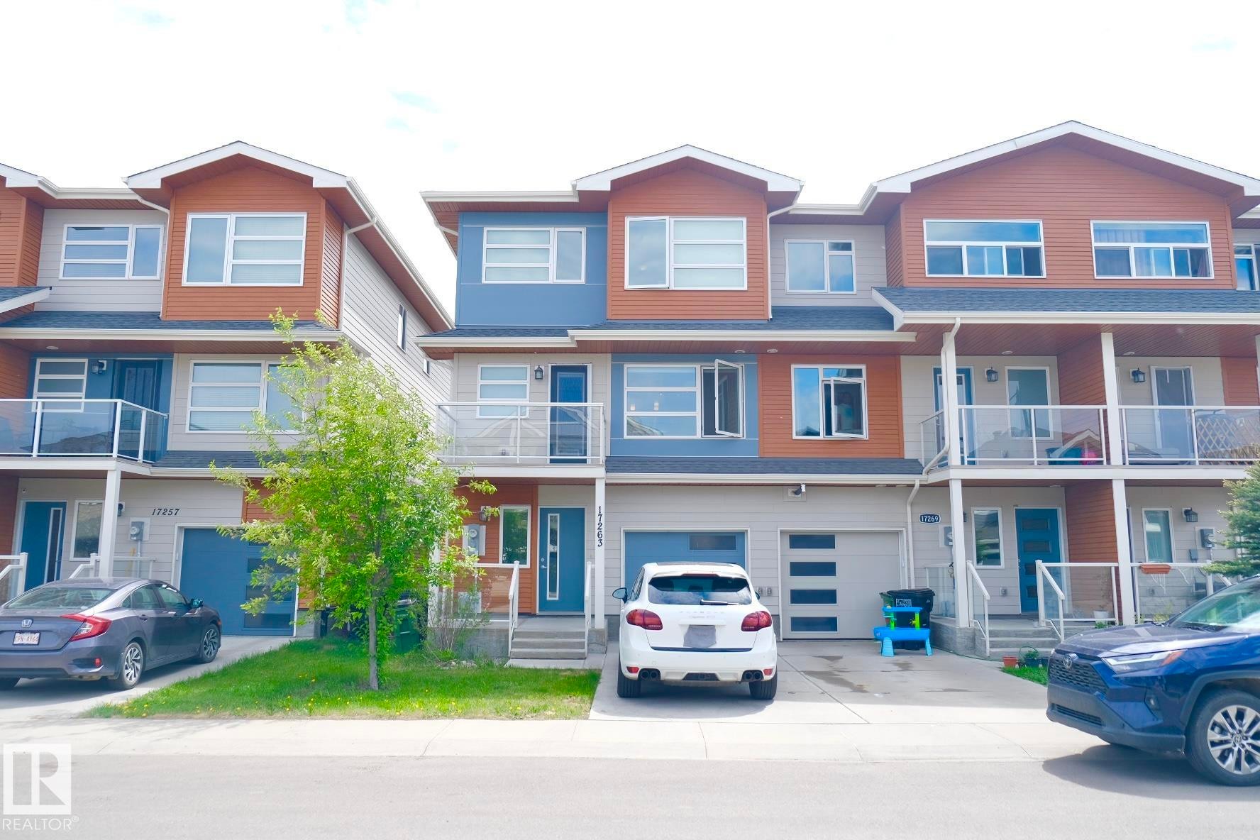 Modern townhome exterior featuring multi-toned siding, a private balcony with glass railings, an integrated garage, a paved driveway, and a covered entry - 17263 9 Avenue Sw, Edmonton, AB