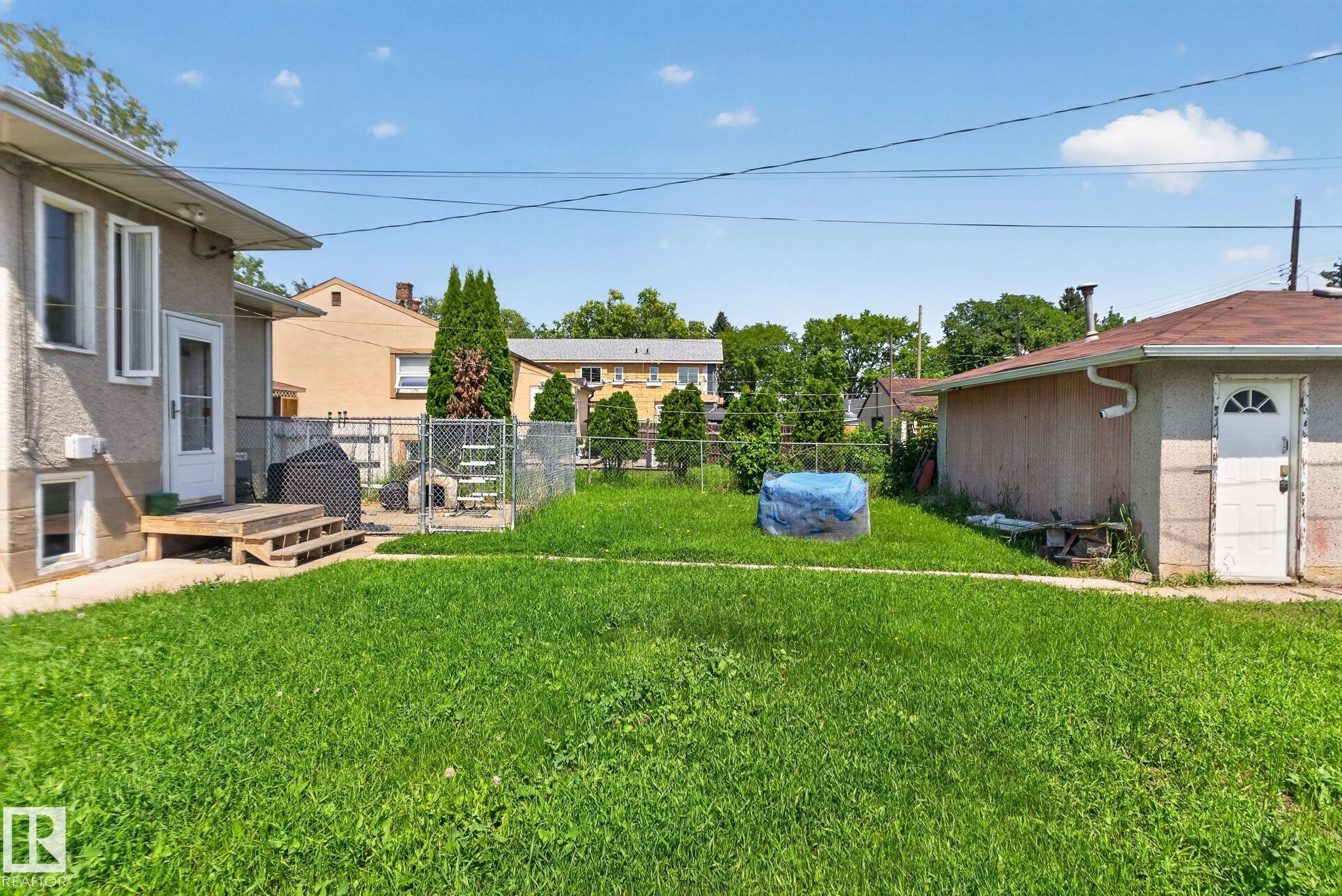 Expansive grassy yard area with a stucco-finish house exterior and a detached garage featuring an arched window door - 12229 88 Street Nw, Edmonton, AB
