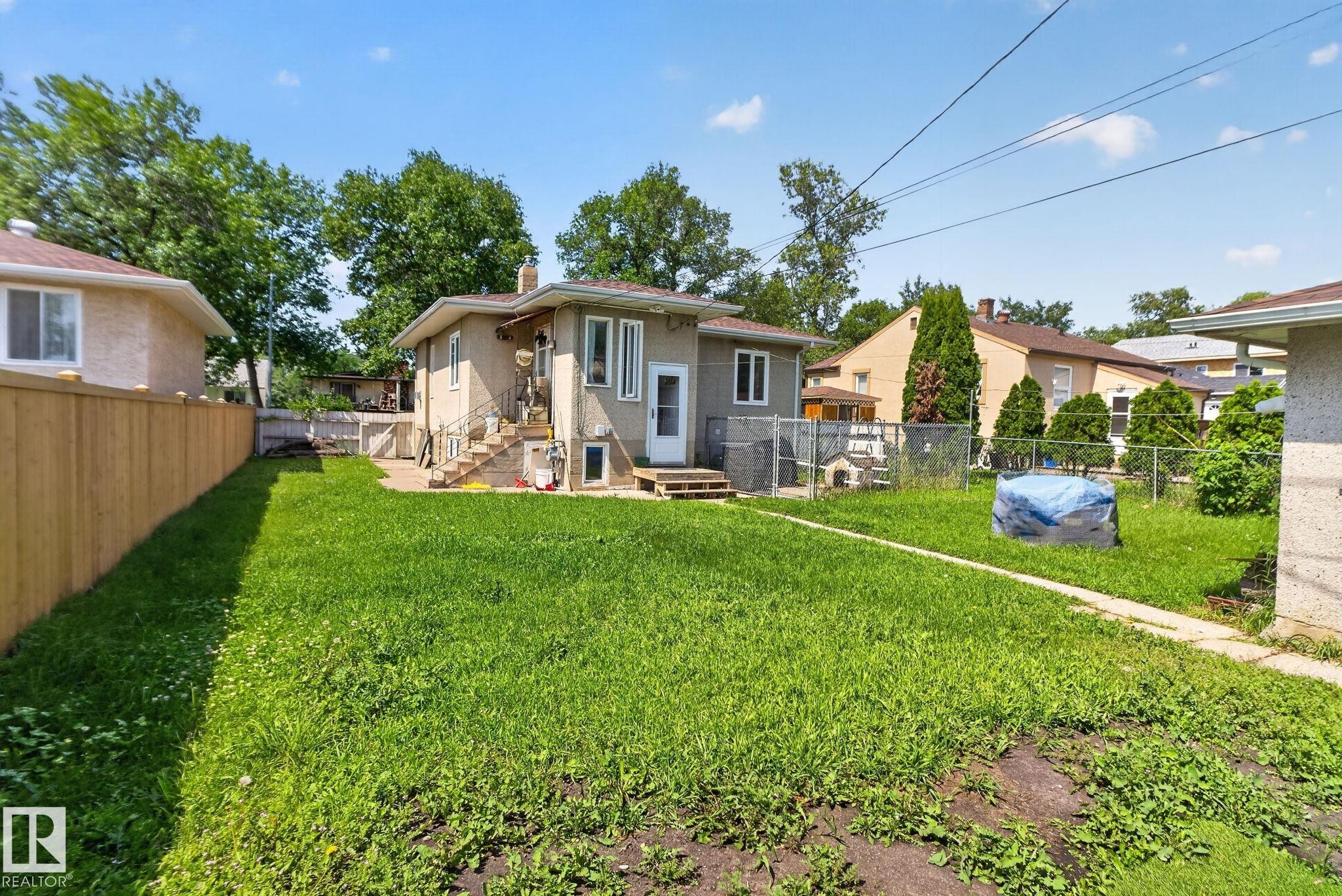 Expansive rear yard featuring a paved walkway, a wood privacy fence, and mature trees - 12229 88 Street Nw, Edmonton, AB