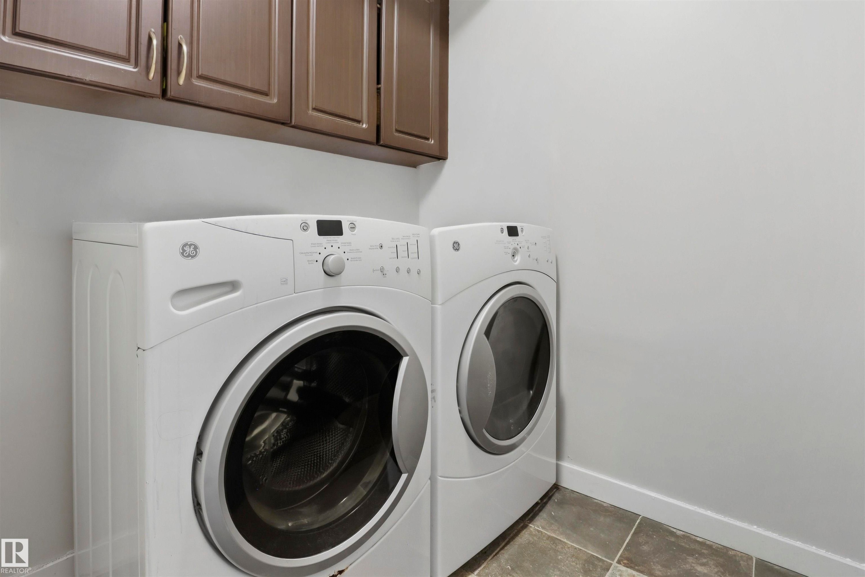 Laundry area featuring neutral wall paint, overhead cabinetry with panel doors and silver-tone hardware, and square floor tiles - 1528 35 Avenue Nw, Edmonton, AB - Indoor Photo Showing Laundry Room