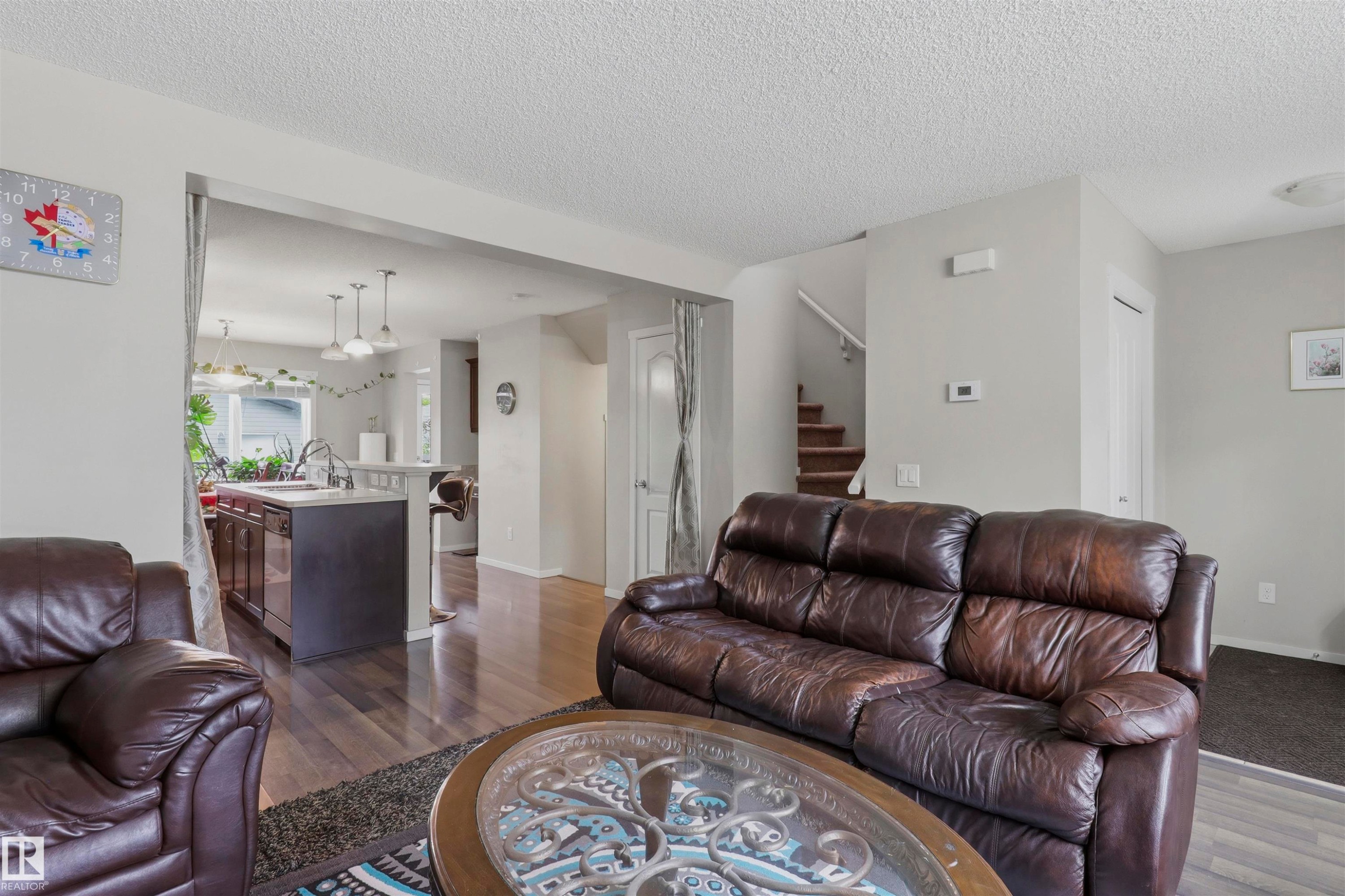 Open-concept living area featuring rich wood-finish flooring, a kitchen island with pendant lighting, and a staircase with a wooden handrail - 1528 35 Avenue Nw, Edmonton, AB - Indoor Photo Showing Living Room
