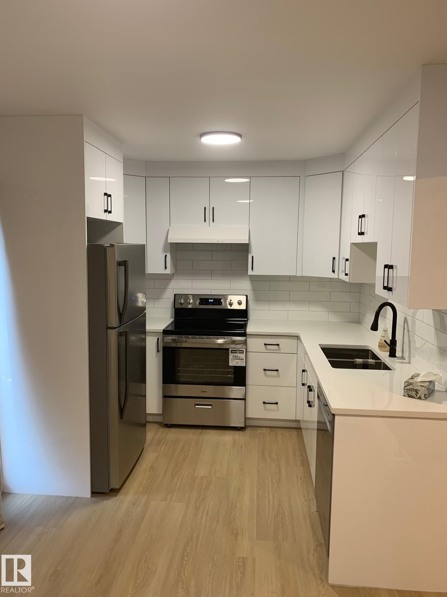 Modern kitchen featuring white cabinetry with dark hardware, stainless steel appliances, a white subway tile backsplash, and light wood-finish flooring - 16321 - 109A Ave Nw, Edmonton, AB - Indoor Photo Showing Kitchen With Double Sink