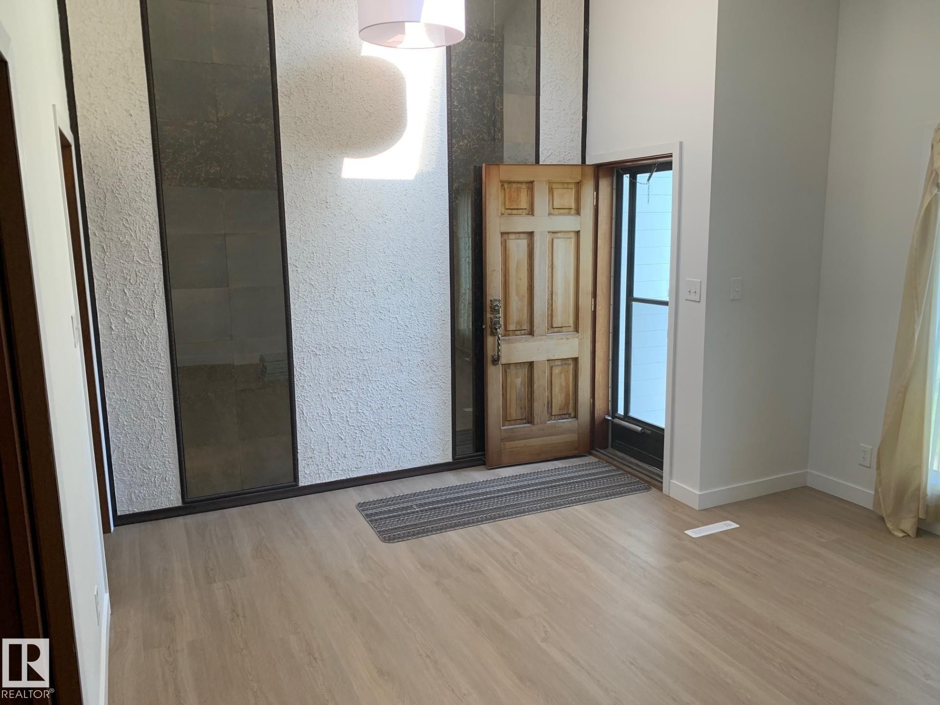 Bright entryway featuring wood-finish flooring, a textured accent wall with dark paneled inserts, and a high ceiling - 16321 - 109A Ave Nw, Edmonton, AB - Indoor