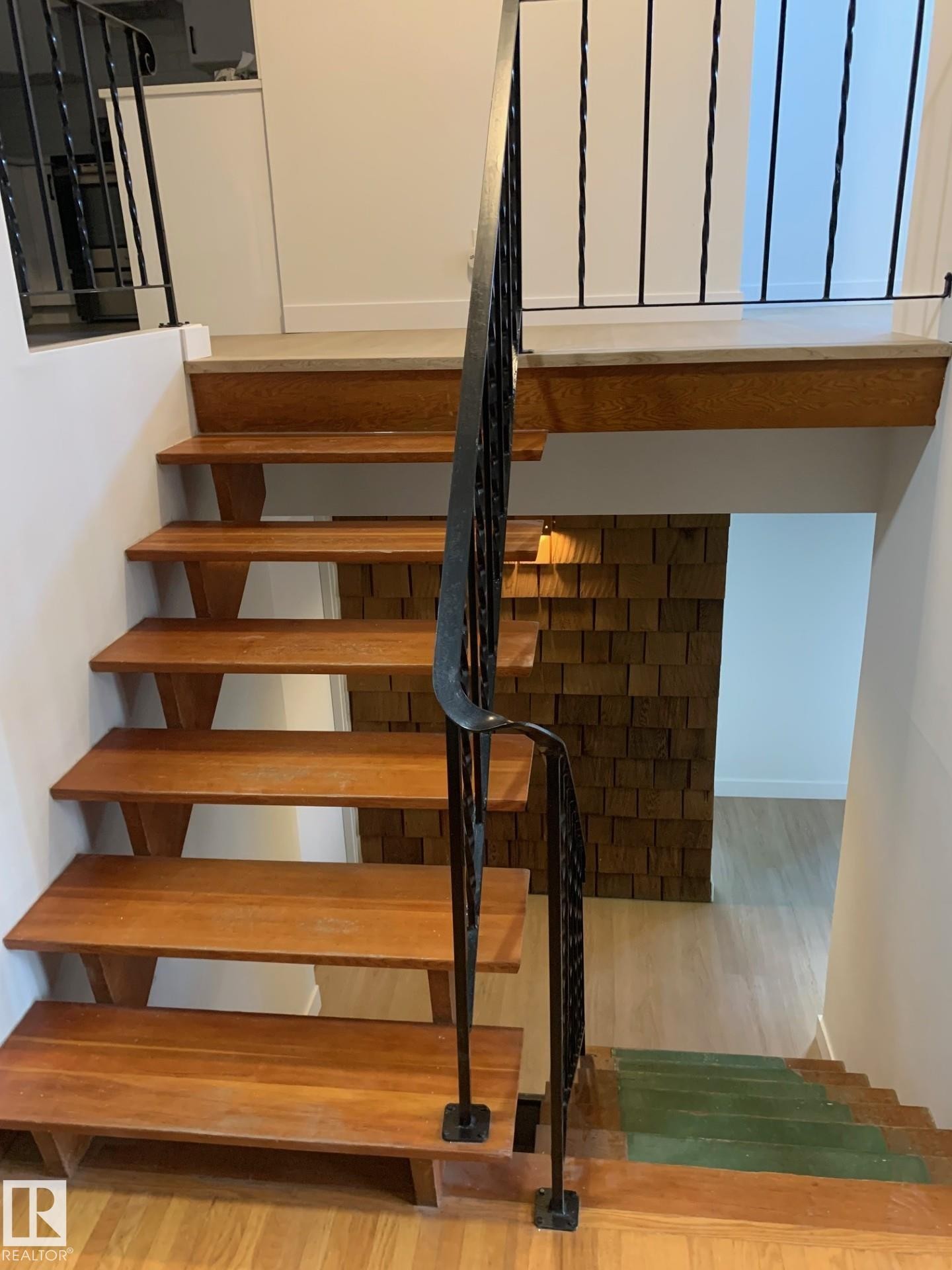 Hardwood staircase featuring a metal handrail, wood-finish flooring, and a unique textured wall accent - 16321 - 109A Ave Nw, Edmonton, AB - Indoor Photo Showing Other Room