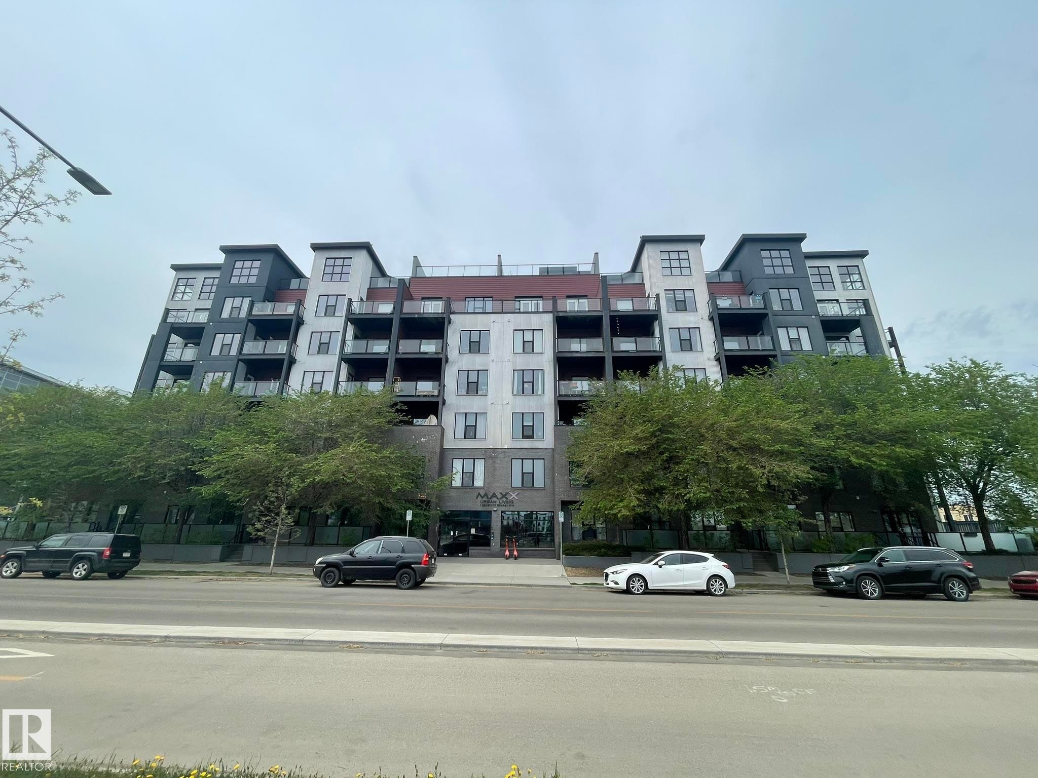 Contemporary multi-story building featuring varied facade materials including light and dark panels, multiple balconies with glass railings, and a prominent ground-level entrance - #504 10518 113 St Nw, Edmonton, AB - Outdoor With Balcony With Facade