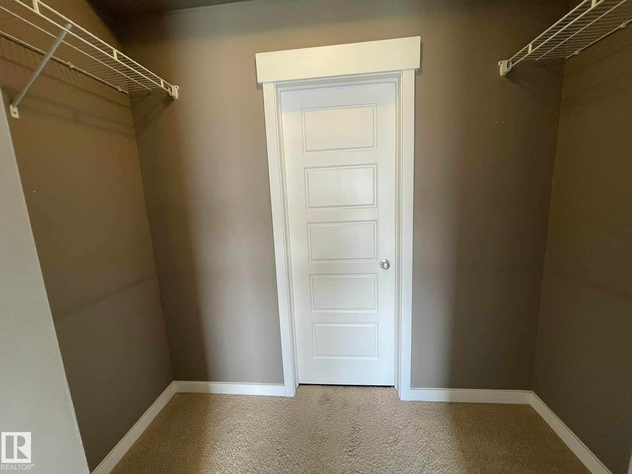 Closet space featuring neutral-toned walls, white wire shelving, a contrasting white paneled door with a silver knob, and light brown carpeting - #504 10518 113 St Nw, Edmonton, AB - Indoor With Storage