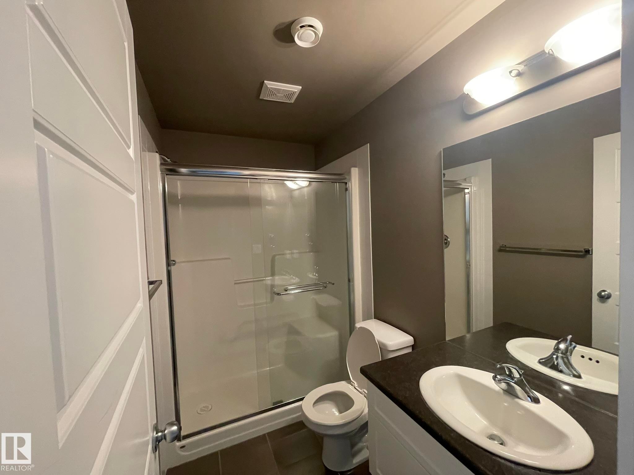 Bathroom featuring a walk-in shower with glass enclosure, white vanity with dual sinks, dark countertop, and dark floor tiles - #504 10518 113 St Nw, Edmonton, AB - Indoor Photo Showing Bathroom