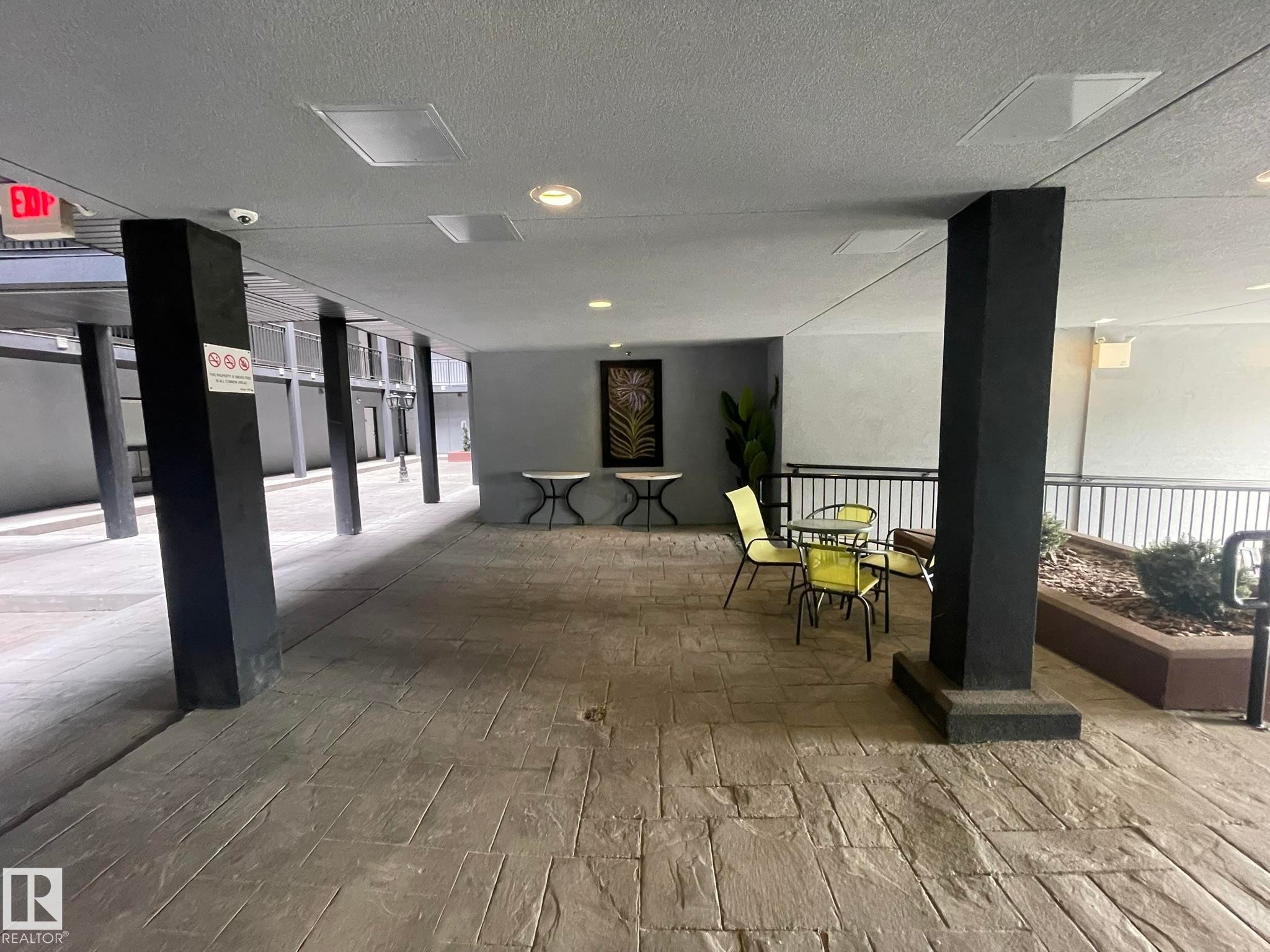 Covered outdoor walkway featuring stamped concrete flooring, black structural columns, recessed lighting, and a decorative planter box with landscaping - #504 10518 113 St Nw, Edmonton, AB - Indoor Photo Showing Other Room