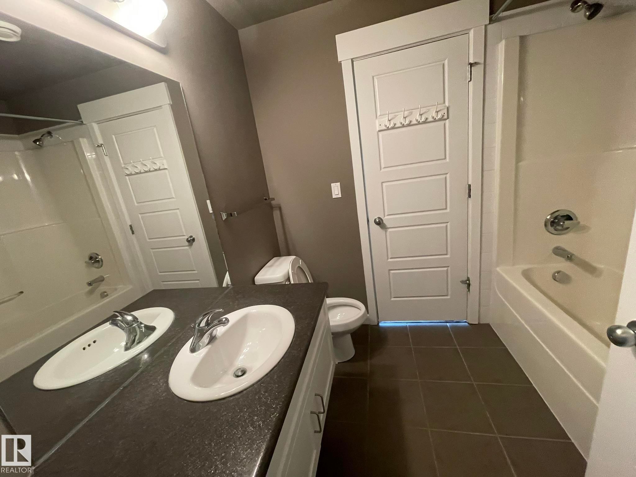 Bathroom featuring a dual-sink vanity with white oval sinks, chrome faucets, and a dark countertop - #504 10518 113 St Nw, Edmonton, AB - Indoor Photo Showing Bathroom