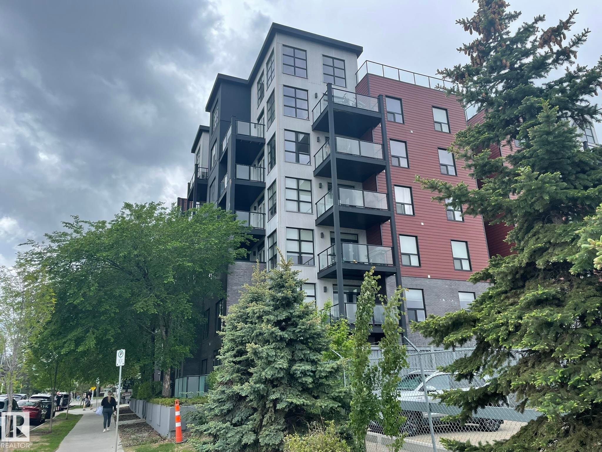 Multi-story building featuring a brick and panel facade, multiple balconies with glass railings, and ground-level commercial frontage - #504 10518 113 St Nw, Edmonton, AB - Outdoor With Balcony