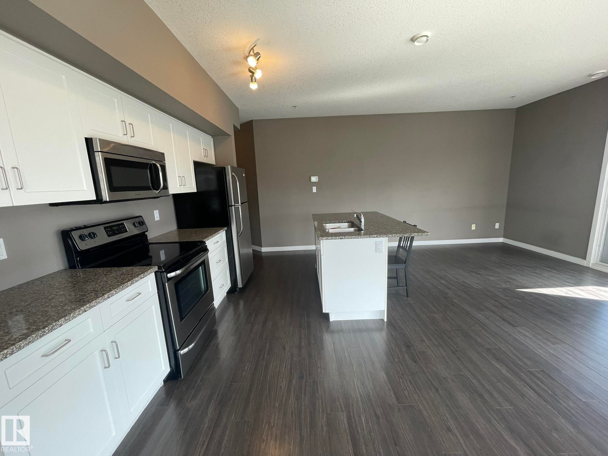 Modern kitchen featuring white cabinetry, stainless steel appliances, granite countertops, and a central island with an undermount sink - #504 10518 113 St Nw, Edmonton, AB - Indoor Photo Showing Kitchen With Stainless Steel Kitchen