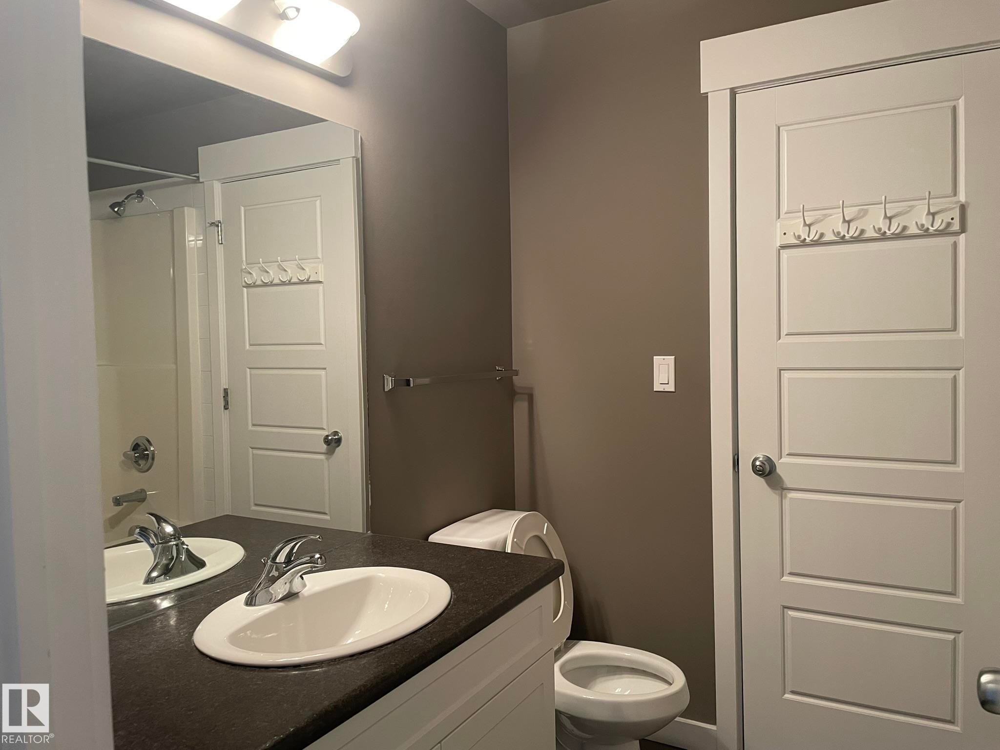 Bathroom vanity featuring an integrated sink with chrome faucet, dark countertop, and white cabinetry - #504 10518 113 St Nw, Edmonton, AB - Indoor Photo Showing Bathroom