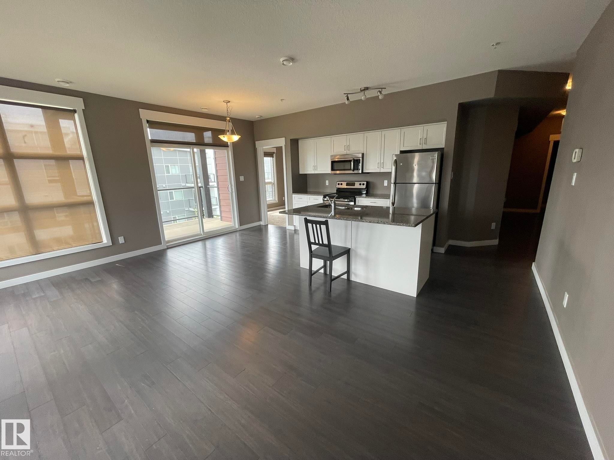 Open-concept living space featuring wood-finish flooring, a kitchen island with stone countertop, stainless steel appliances, white cabinetry, and a balcony with sliding glass doors - #504 10518 113 St Nw, Edmonton, AB - Indoor Photo Showing Kitchen