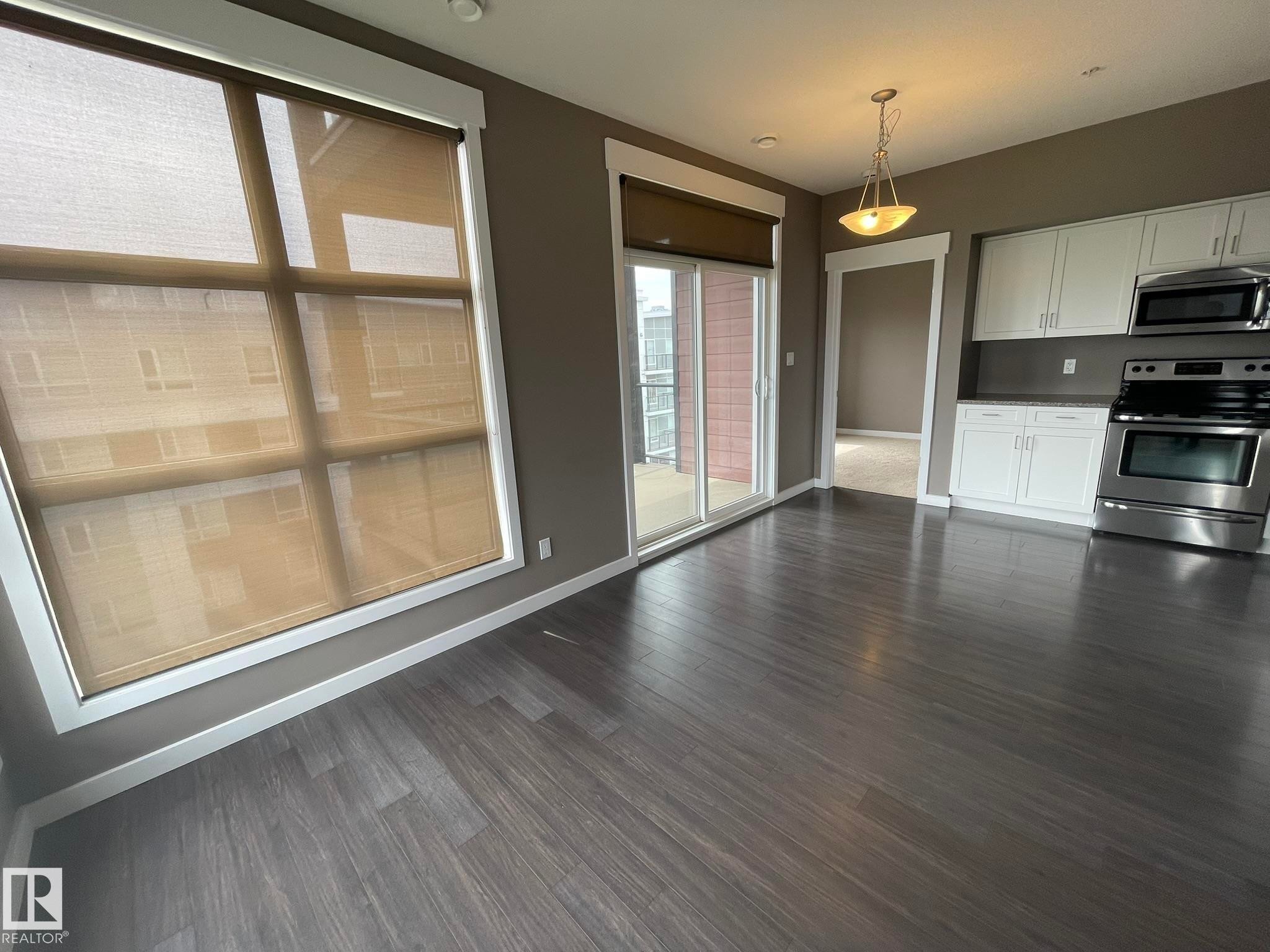Open-concept living area featuring wood-finish flooring, a full kitchen with white cabinetry and stainless steel appliances, and a sliding glass door leading to a balcony - #504 10518 113 St Nw, Edmonton, AB - Indoor Photo Showing Kitchen