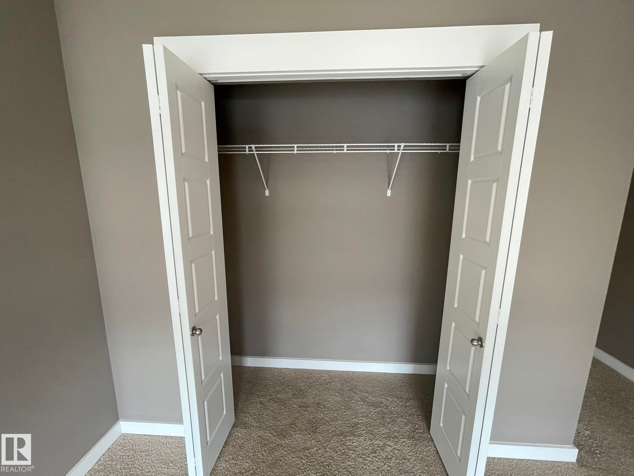 Reach-in closet featuring bi-fold panel doors, a single wire shelving unit, and carpet flooring - #504 10518 113 St Nw, Edmonton, AB - Indoor