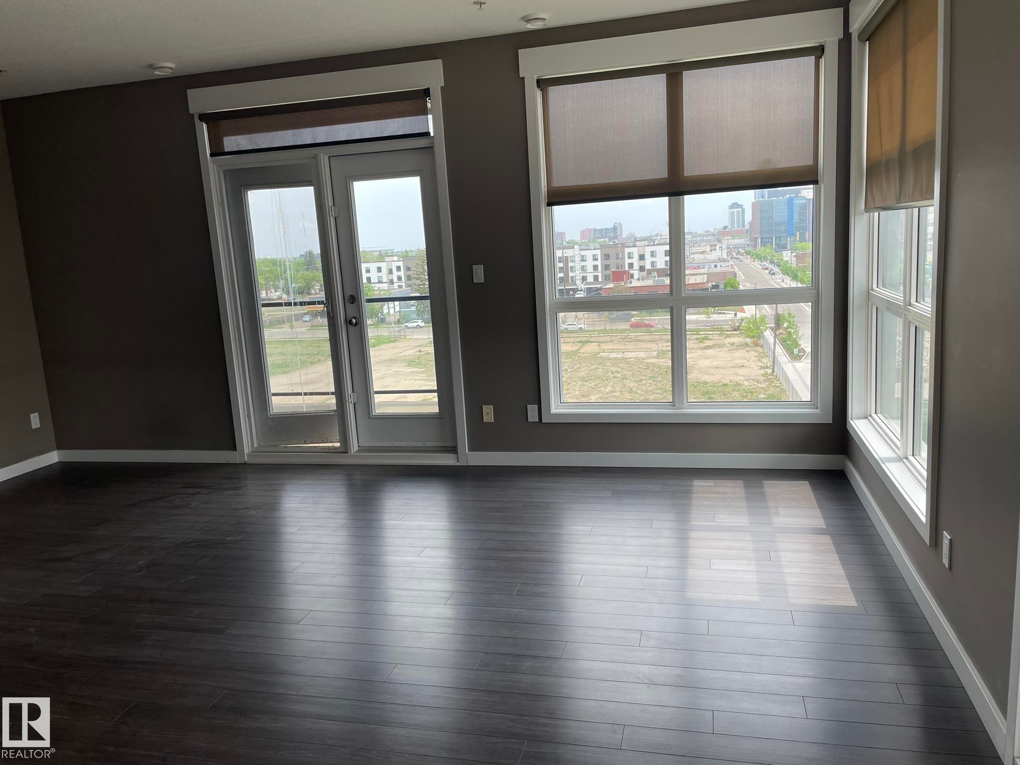 Spacious interior featuring dark wood-finish flooring, neutral gray walls, and white baseboards - #504 10518 113 St Nw, Edmonton, AB - Indoor Photo Showing Other Room