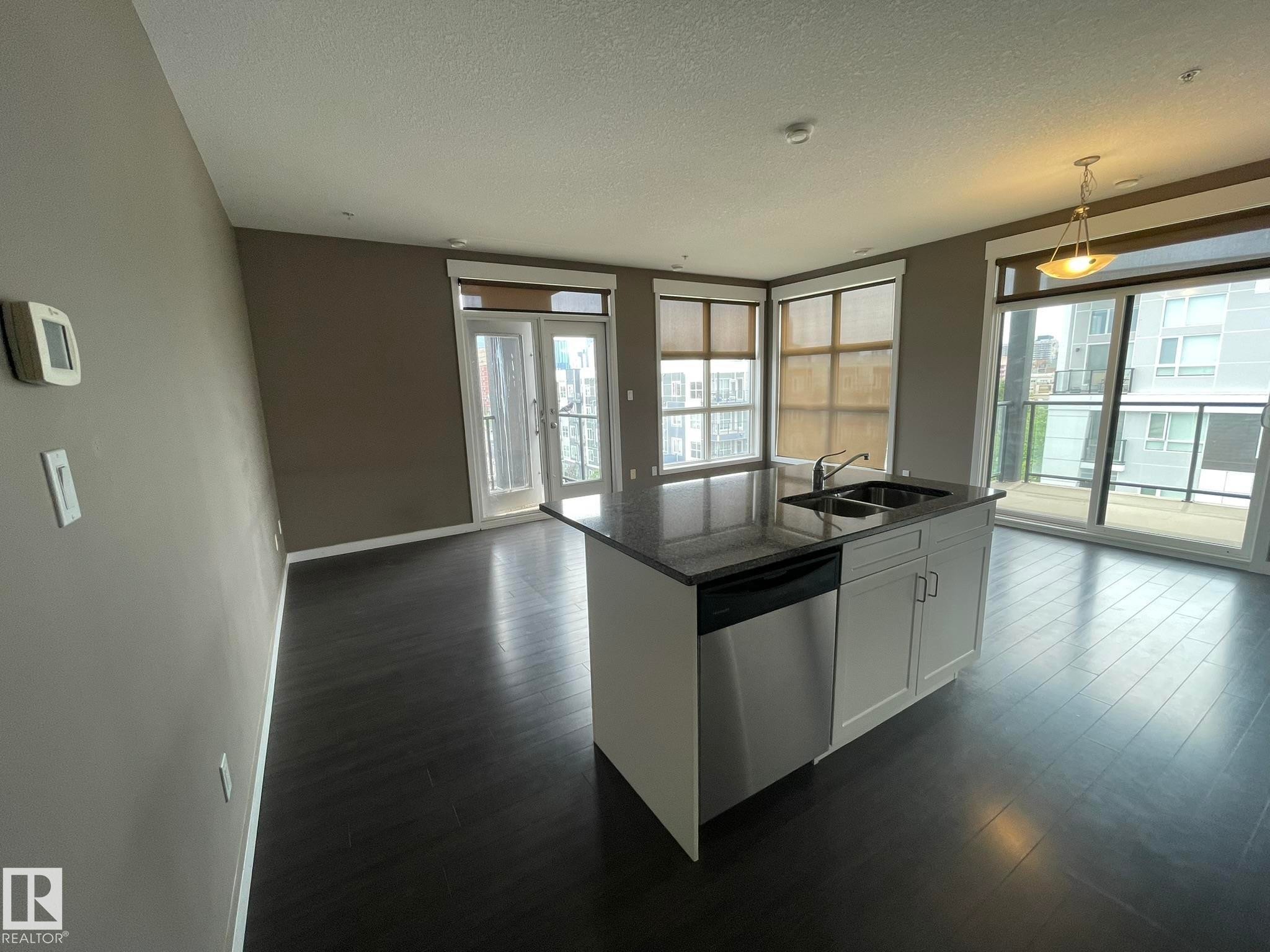 Modern kitchen island with a dark countertop, undermount double sink, and integrated stainless steel dishwasher - #504 10518 113 St Nw, Edmonton, AB - Indoor Photo Showing Kitchen With Double Sink