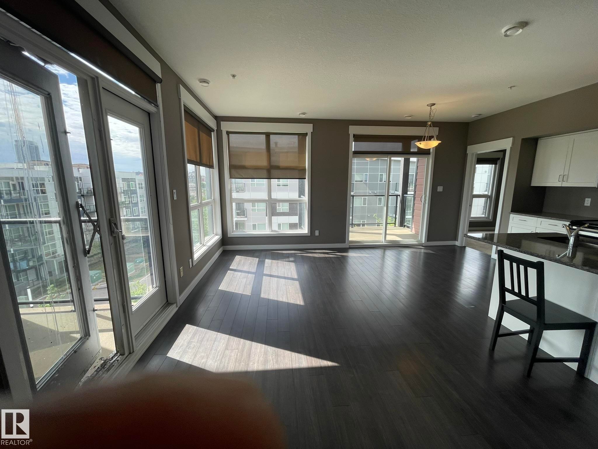 Open-concept living area with dark wood-finish flooring, multiple large windows, and direct access to a balcony - #504 10518 113 St Nw, Edmonton, AB - Indoor