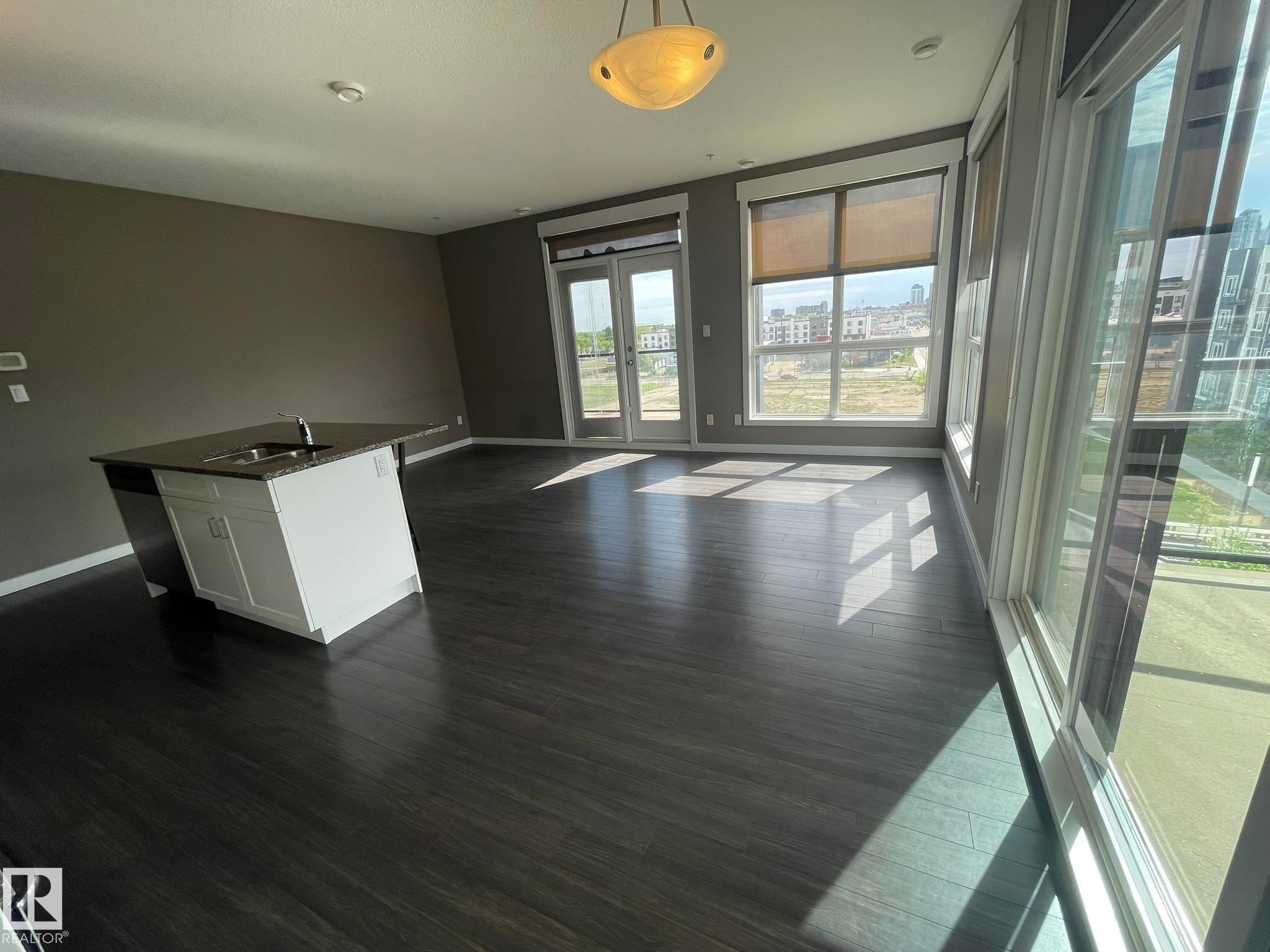 Open-concept living area featuring dark wood-finish flooring, abundant natural light from large windows, and a built-in island with a sink and dark countertop - #504 10518 113 St Nw, Edmonton, AB - Indoor Photo Showing Other Room