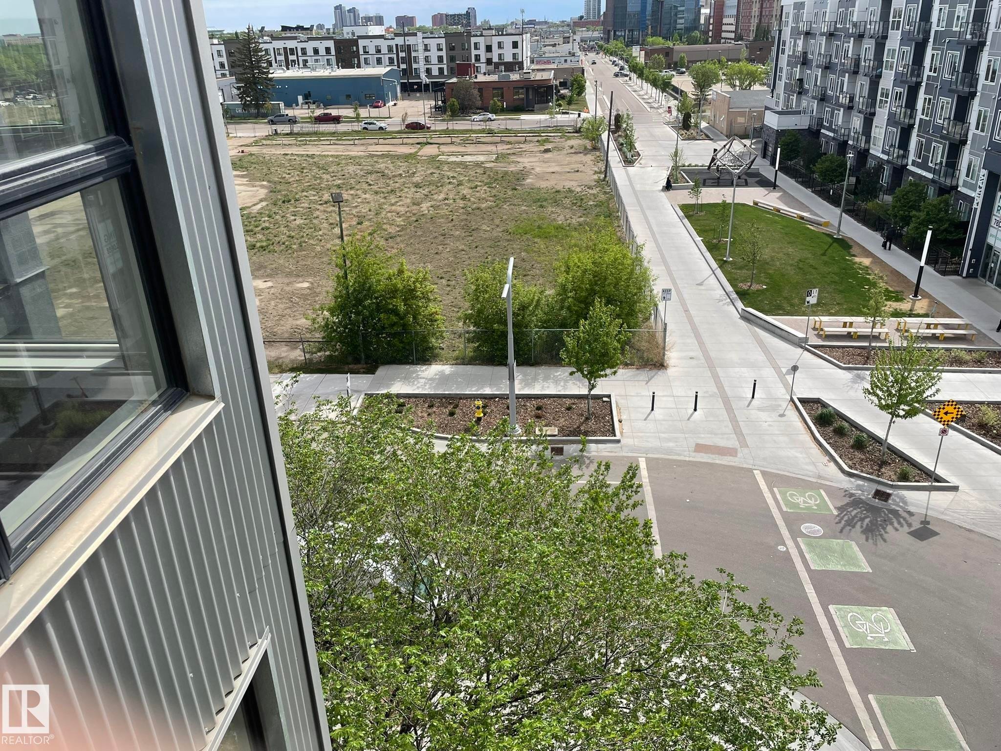 Urban streetscape featuring a paved roadway with painted bicycle lane markings, a pedestrian promenade, and landscaped green spaces - #504 10518 113 St Nw, Edmonton, AB - Outdoor