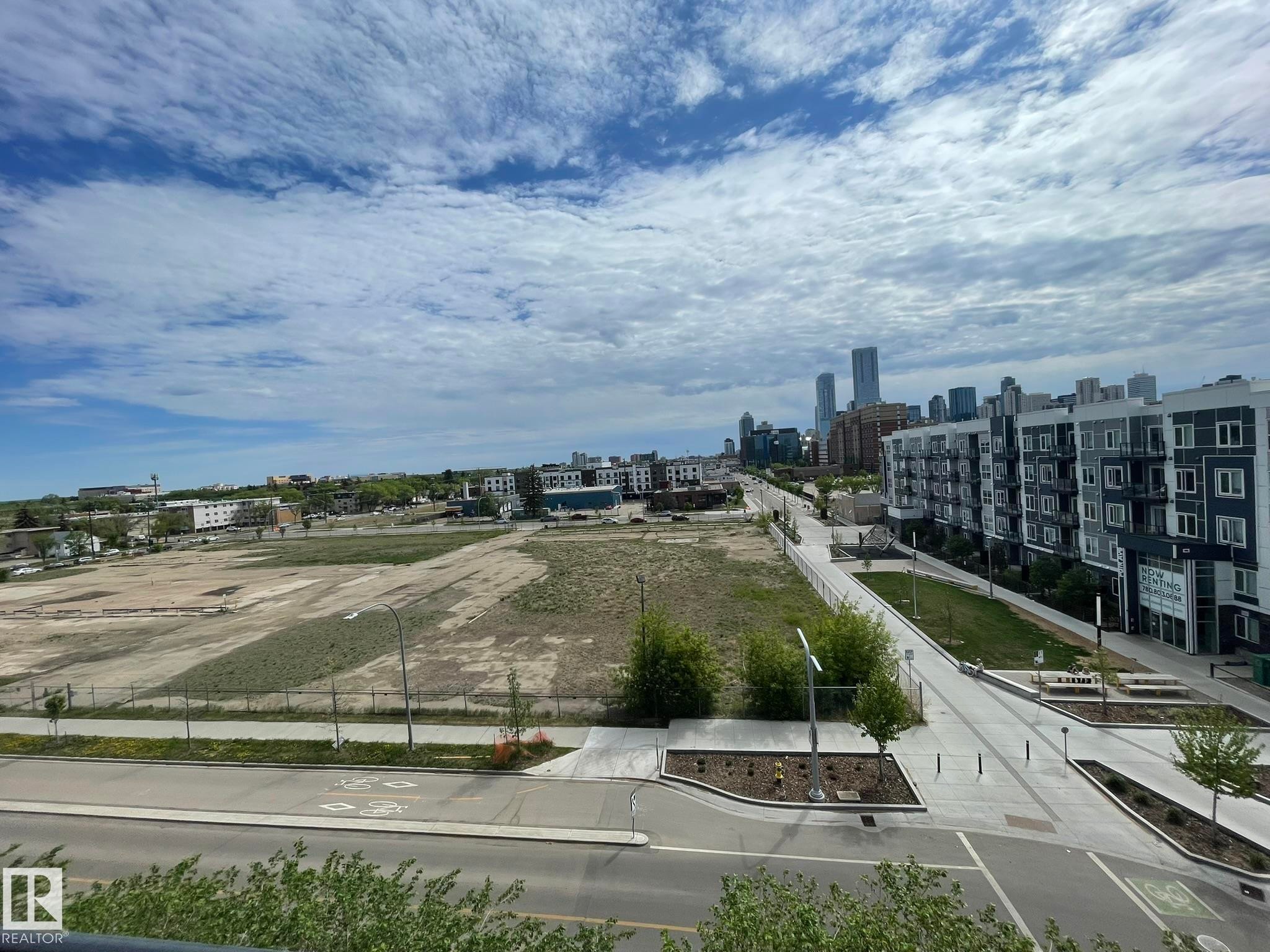 Urban landscape featuring a distant city skyline, multi-story residential buildings with balconies, paved roadways, and undeveloped land parcels - #504 10518 113 St Nw, Edmonton, AB - Outdoor With View