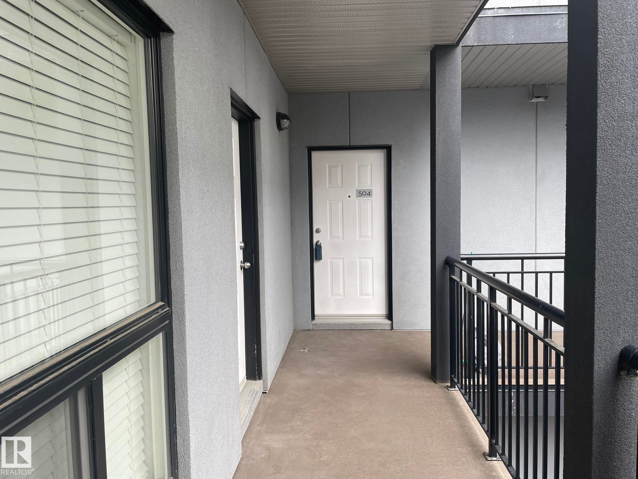 Entryway featuring a solid panel door with transom, textured exterior walls, and a black metal railing - #504 10518 113 St Nw, Edmonton, AB - Outdoor With Exterior