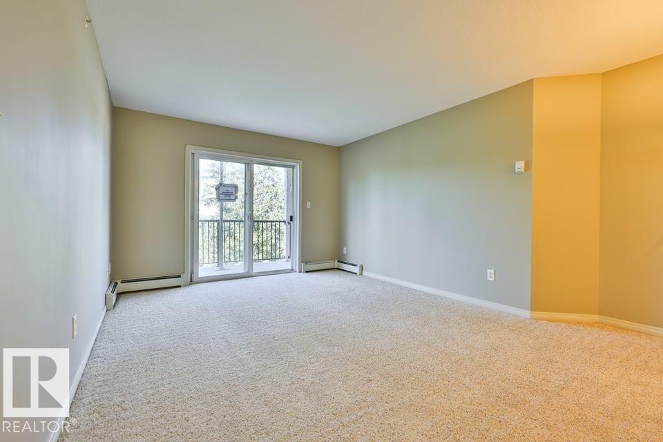 Spacious room featuring neutral carpeting, light-toned walls, and a sliding glass door leading to an outdoor balcony with metal railings - #406 4903 47 Av, Stony Plain, AB - Indoor Photo Showing Other Room