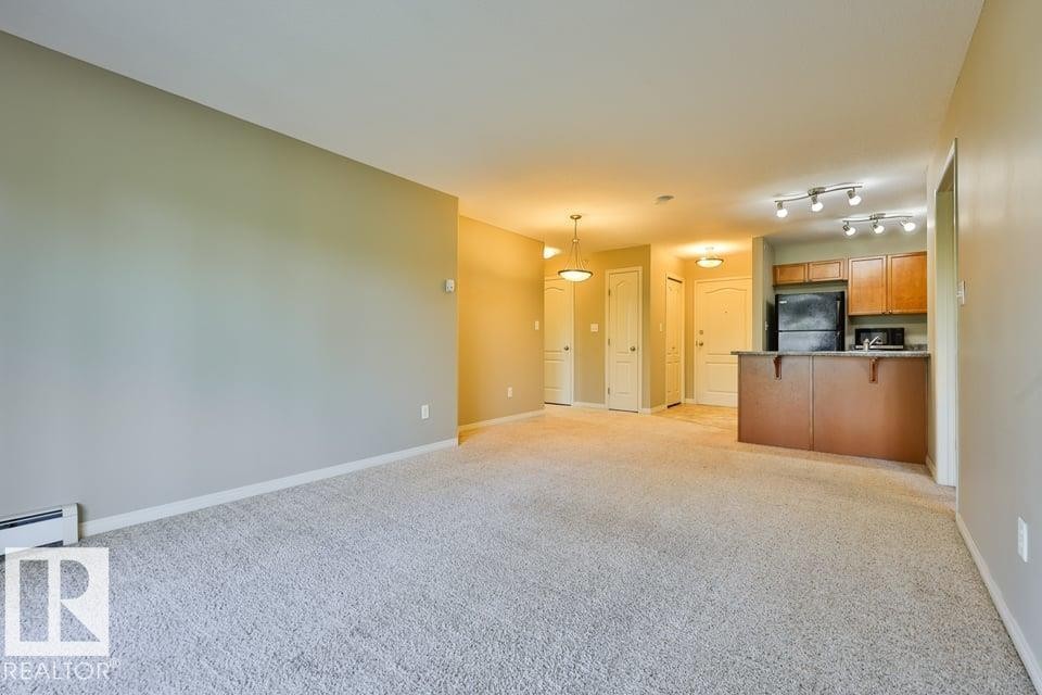 Spacious open-concept living area featuring light-toned carpeting and neutral wall colors - #406 4903 47 Av, Stony Plain, AB - Indoor