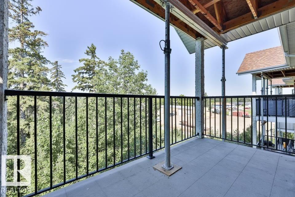 Balcony featuring a black metal railing, textured patio flooring, and exposed wood ceiling - #406 4903 47 Av, Stony Plain, AB - Outdoor With Exterior