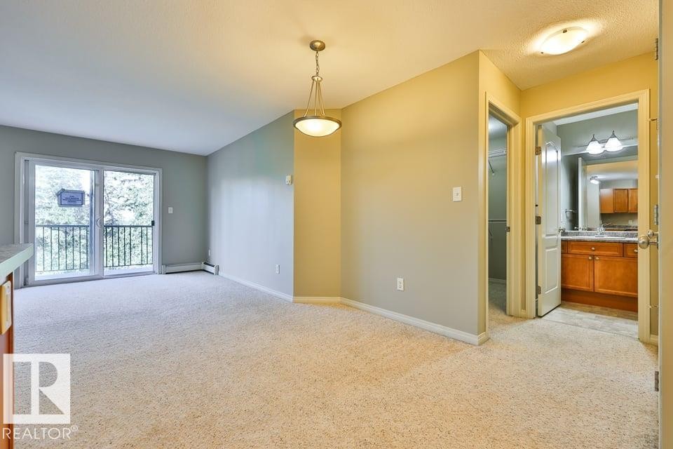 Open-concept living area featuring light-toned carpeting, a sliding glass door with balcony access, and a contemporary pendant light fixture - #406 4903 47 Av, Stony Plain, AB - Indoor Photo Showing Other Room
