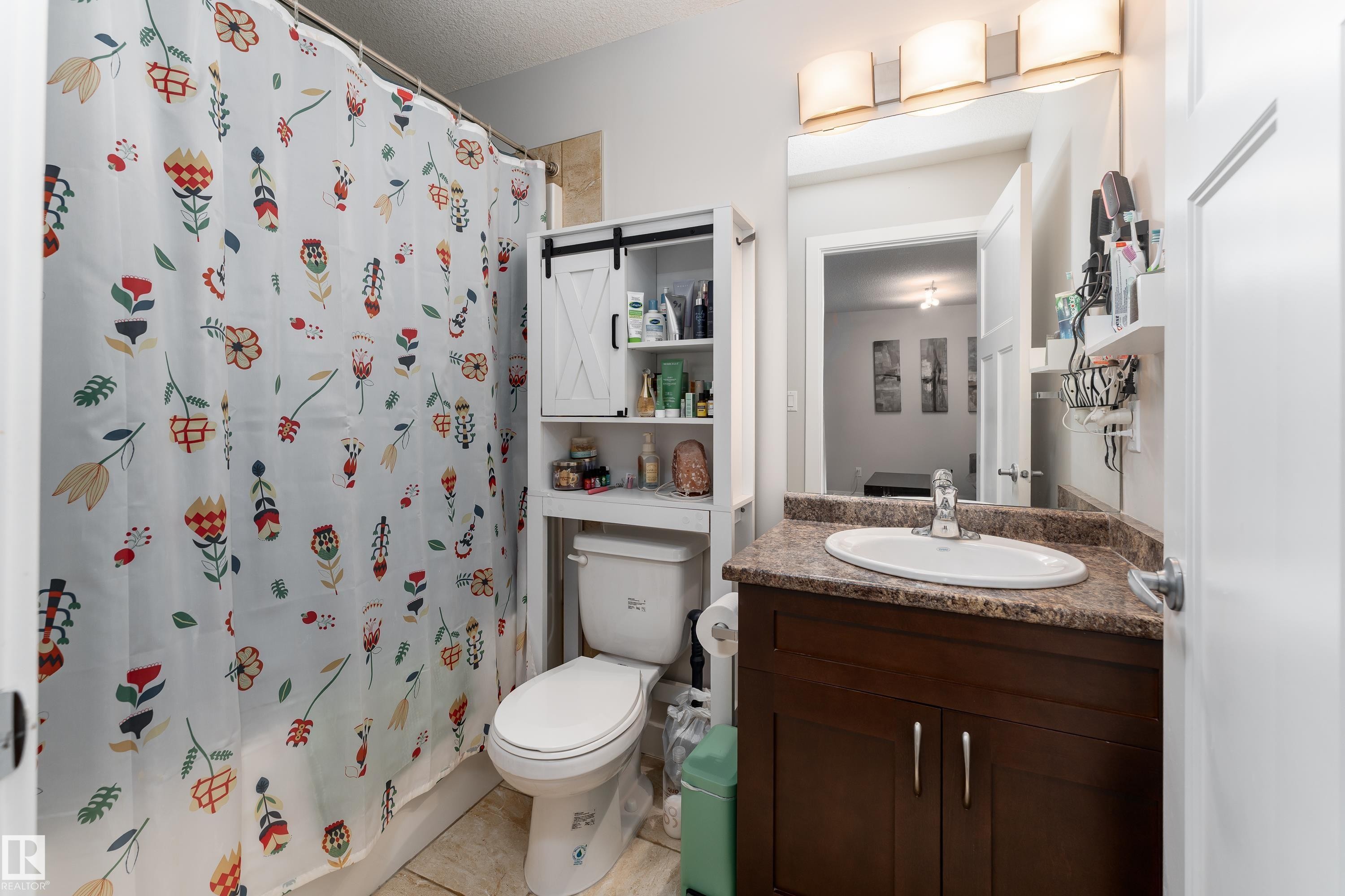 Bathroom featuring a dark wood-finish vanity with a stone-look countertop, an oval undermount sink, and a large mirror - 16805 55 Street Nw, Edmonton, AB - Indoor Photo Showing Bathroom