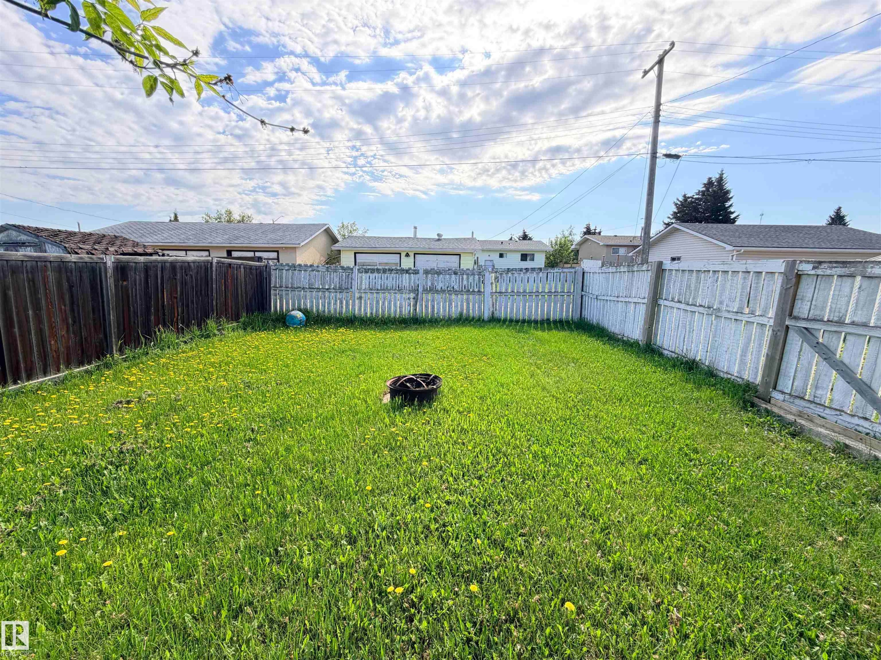 Expansive backyard featuring a green lawn, wood fence perimeter, and a fire pit - 4823 49 Street, Clyde, AB - Outdoor