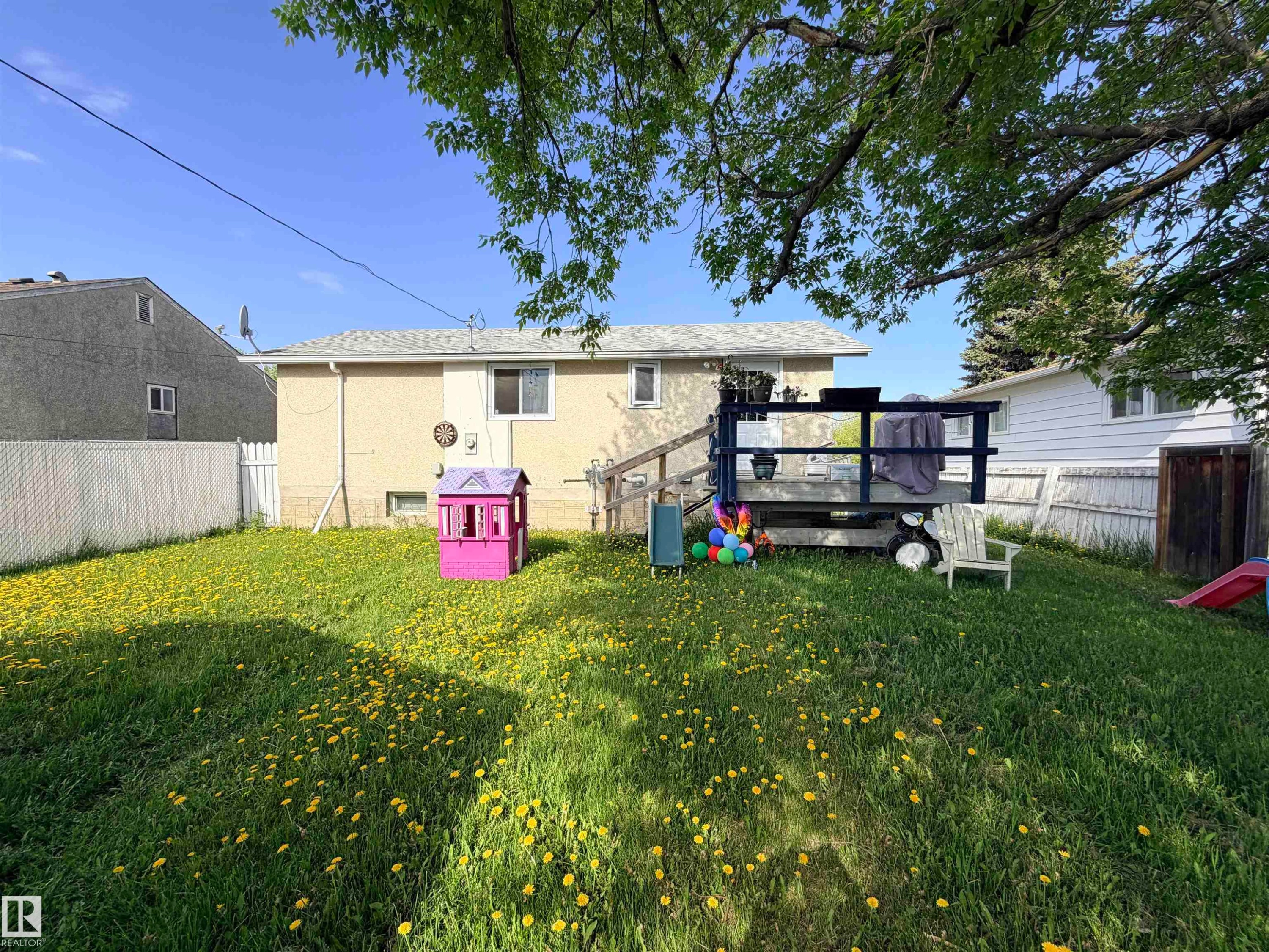 Expansive backyard featuring green lawn, mature trees, and a raised wooden deck with railings - 4823 49 Street, Clyde, AB - Outdoor With Deck Patio Veranda