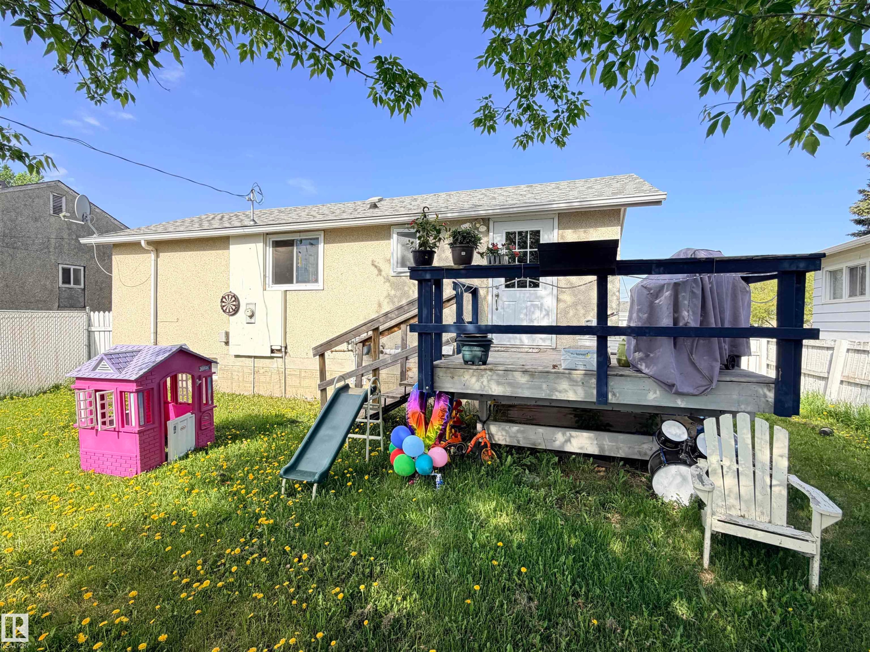 Rear exterior featuring an elevated deck with wood railings, a white paneled door, and multiple windows - 4823 49 Street, Clyde, AB - Outdoor