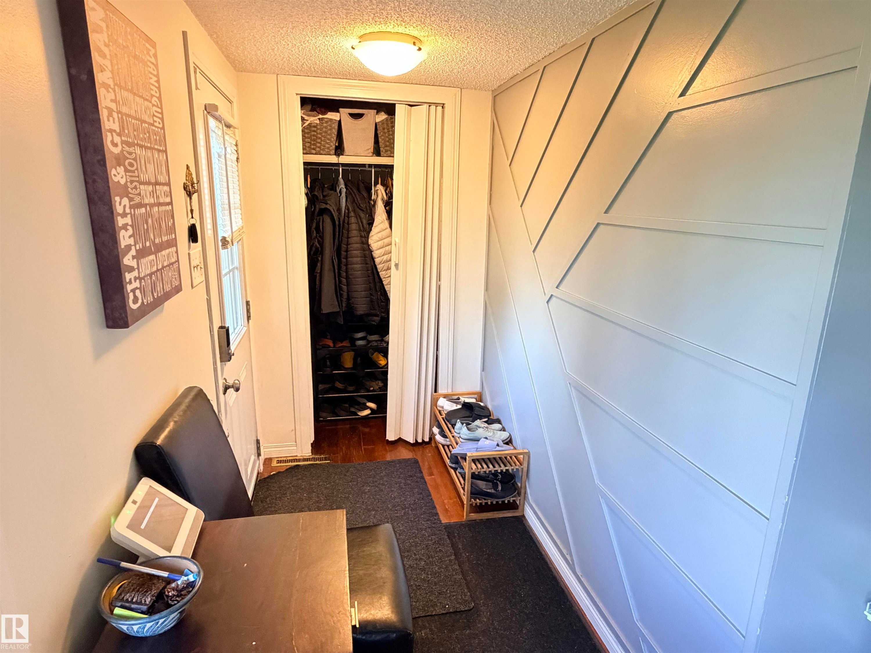 Entryway featuring a decorative accent wall, a built-in closet with bifold doors, and wood-finish flooring - 4823 49 Street, Clyde, AB - Indoor Photo Showing Other Room
