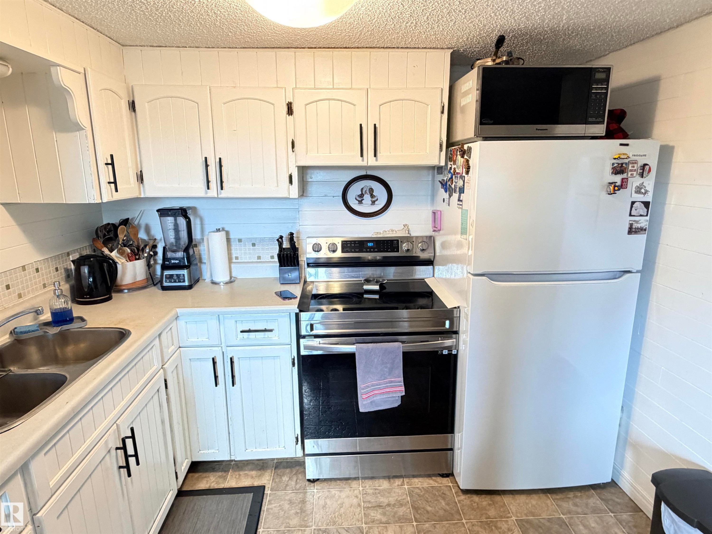 White kitchen cabinetry with black hardware, complementing a stainless steel range and a double basin sink - 4823 49 Street, Clyde, AB - Indoor Photo Showing Kitchen With Double Sink