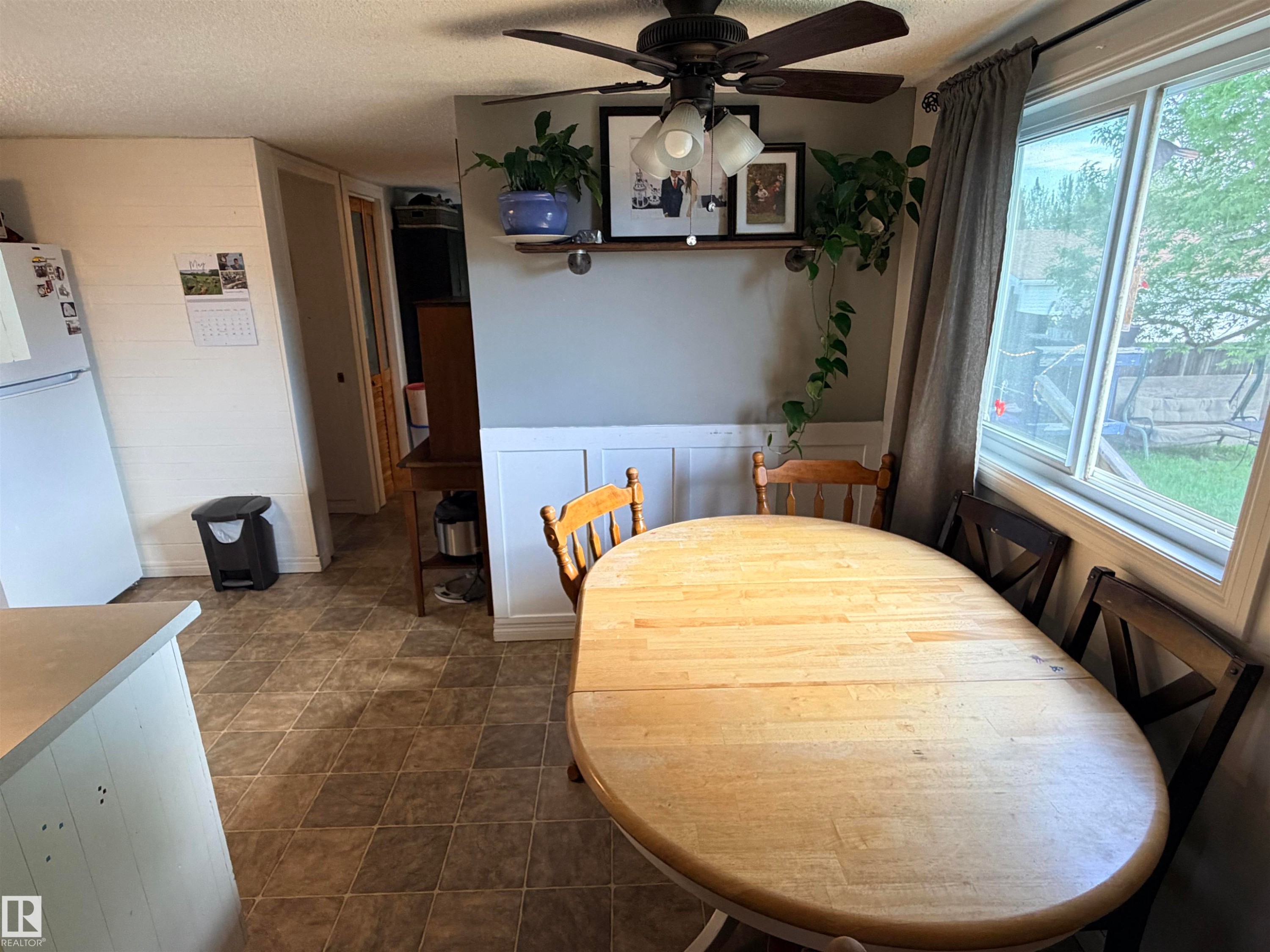 Kitchen area featuring tile-look flooring, a white refrigerator, a corner window, and a ceiling fan with integrated lighting - 4823 49 Street, Clyde, AB - Indoor Photo Showing Dining Room