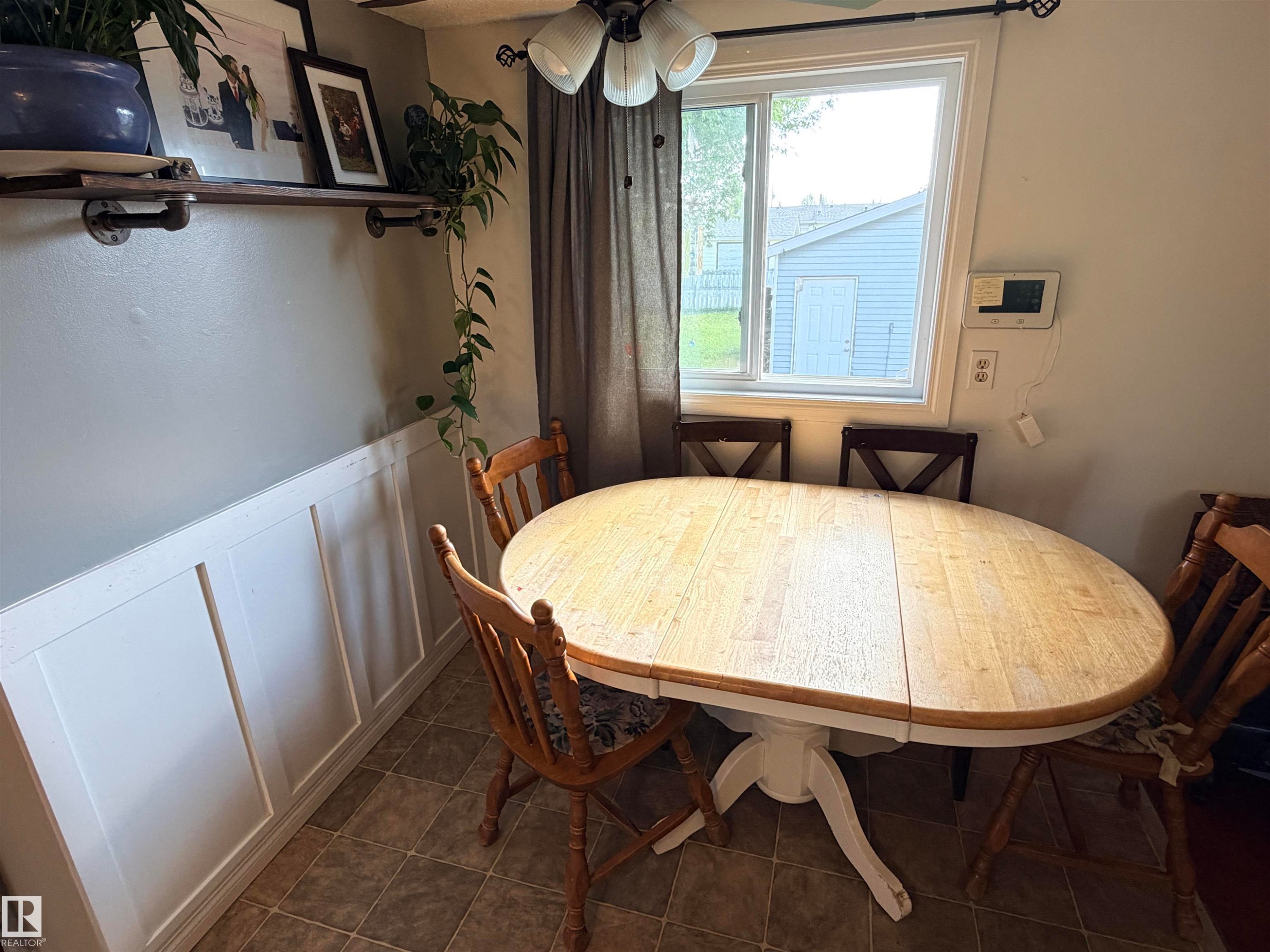 Defined dining area featuring a paneled wainscoting accent wall and a window with a ceiling fan overhead - 4823 49 Street, Clyde, AB - Indoor Photo Showing Dining Room