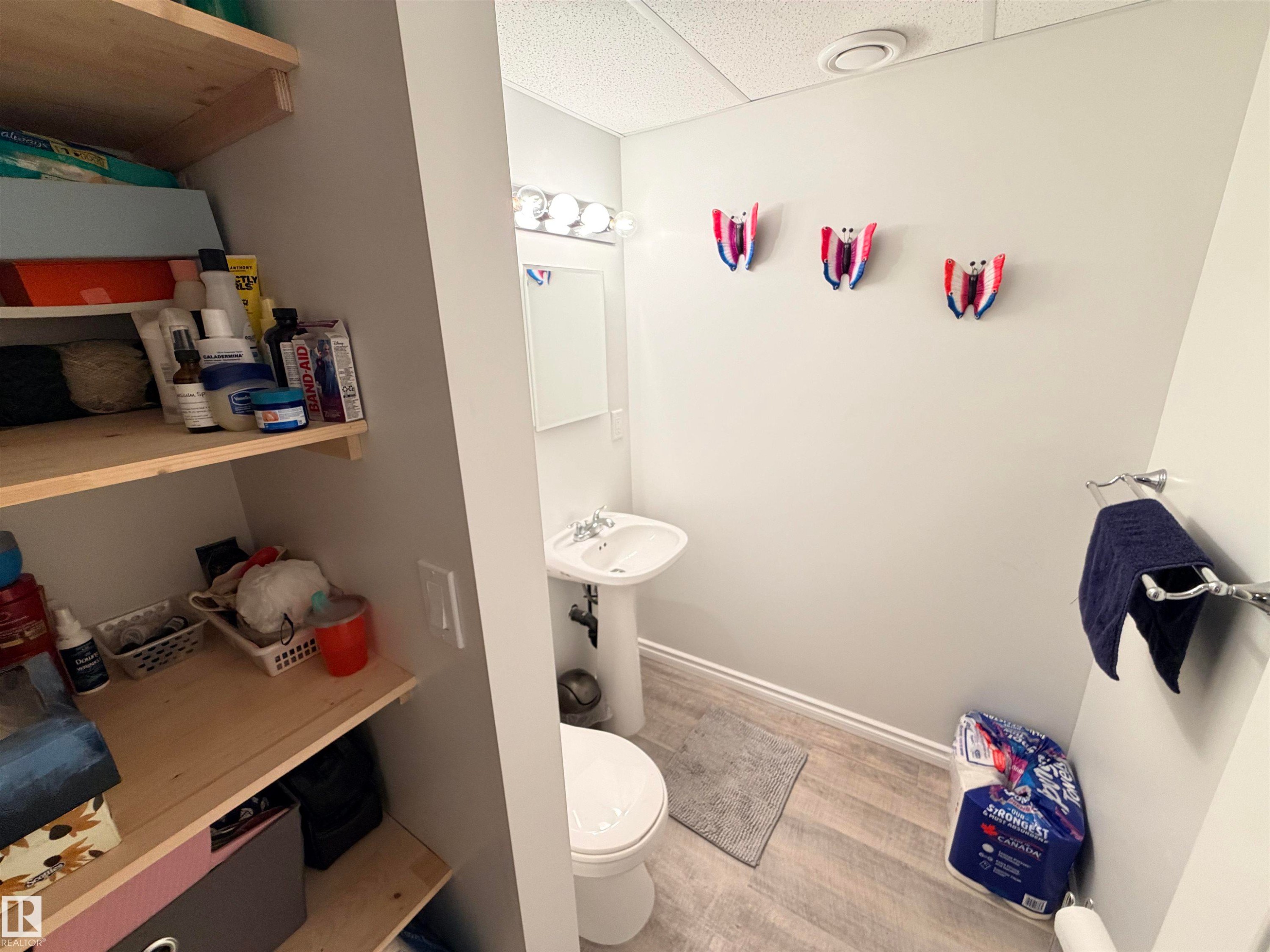 Compact bathroom featuring a pedestal sink, a toilet, a vanity light fixture, and wood-finish flooring - 4823 49 Street, Clyde, AB - Indoor Photo Showing Bathroom